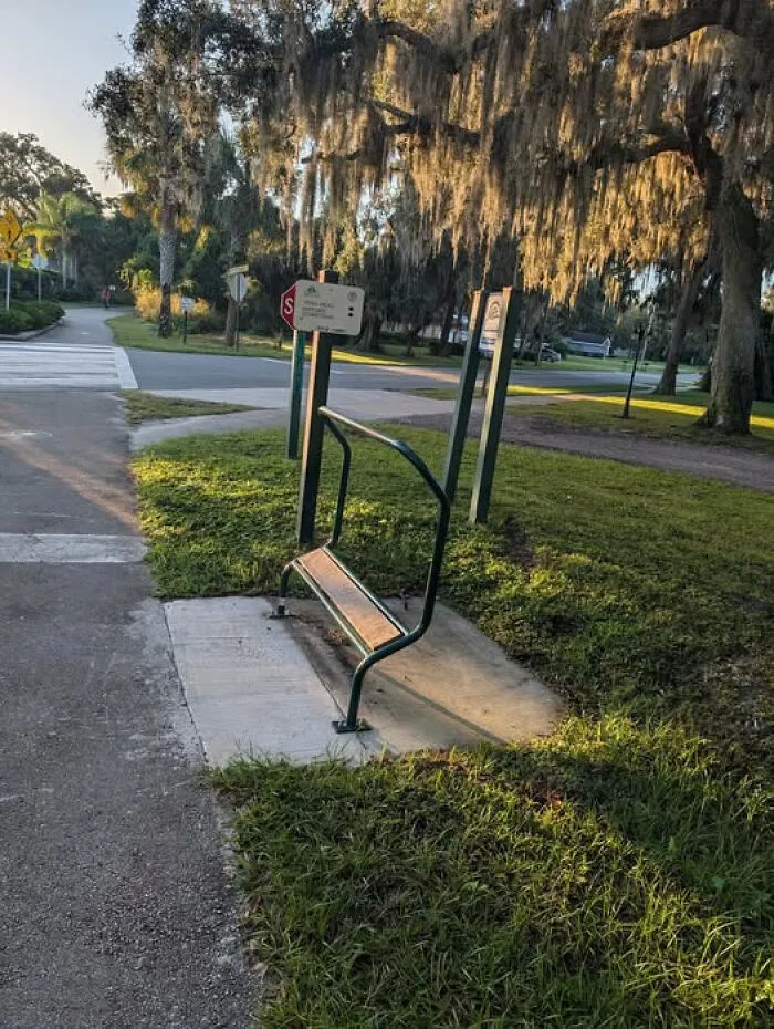 Unidentified object resembling a partial bench in a park setting with trees and street signs in the background.