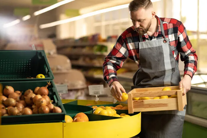Man in plaid shirt and apron arranging lemons in a box at a grocery store produce section, haunted places concept.