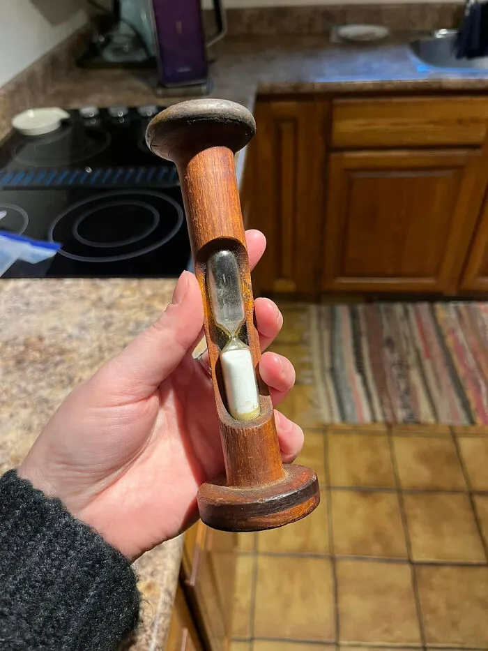 Hand holding a wooden timer with hourglass, one of the unidentified objects the internet solved in a mystery collection.