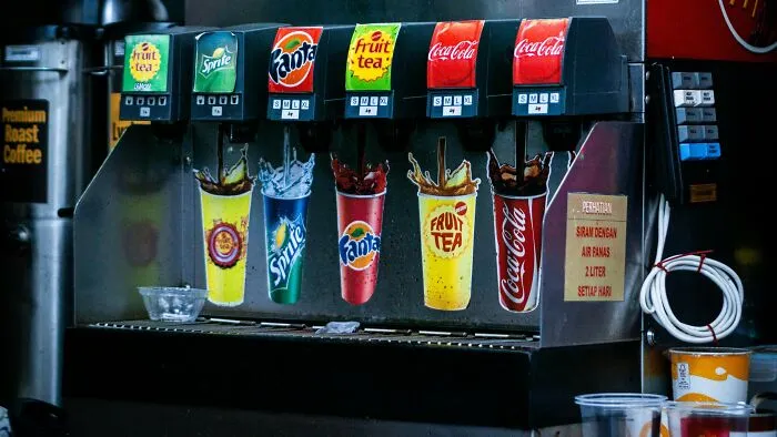 Soda fountain machine pouring various drinks including Sprite, Fanta, Coca-Cola, and fruit tea in a beverage dispenser.
