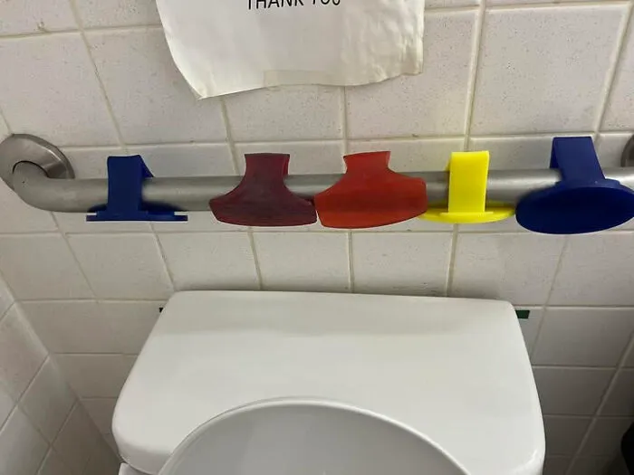 Colorful unidentified objects hung on a bathroom wall grab bar, featuring various shapes and sizes in a tiled restroom.
