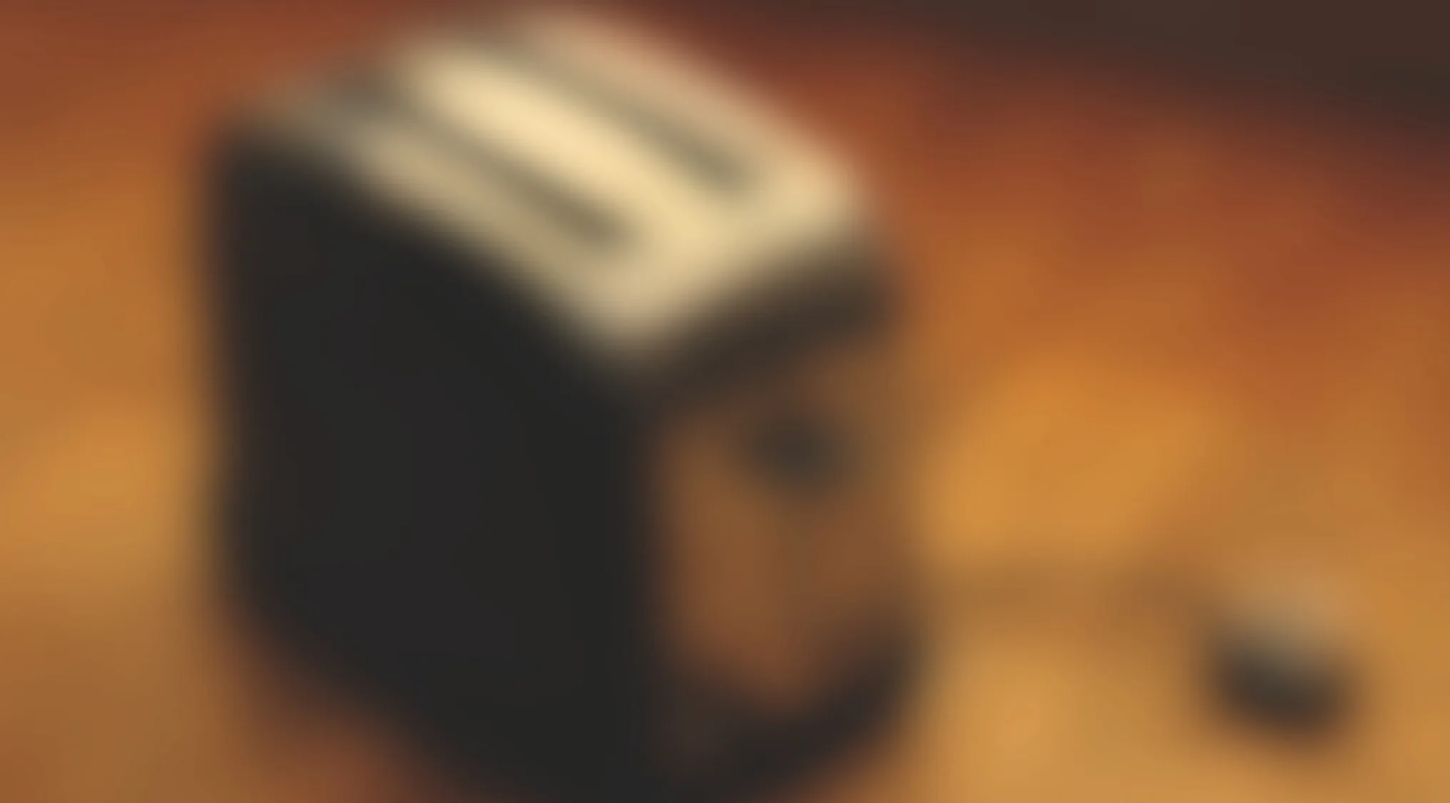 Blurry kitchen appliance on a wooden surface, hinting at a common breakfast device behind the blur.