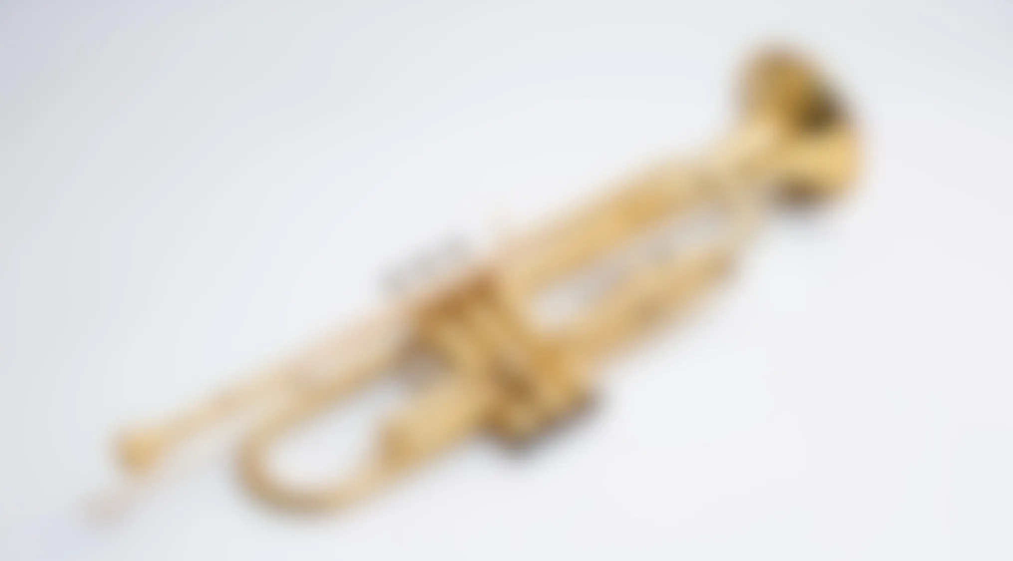 Blurry image of a brass trumpet on a light background, challenging viewers to make out the object clearly.