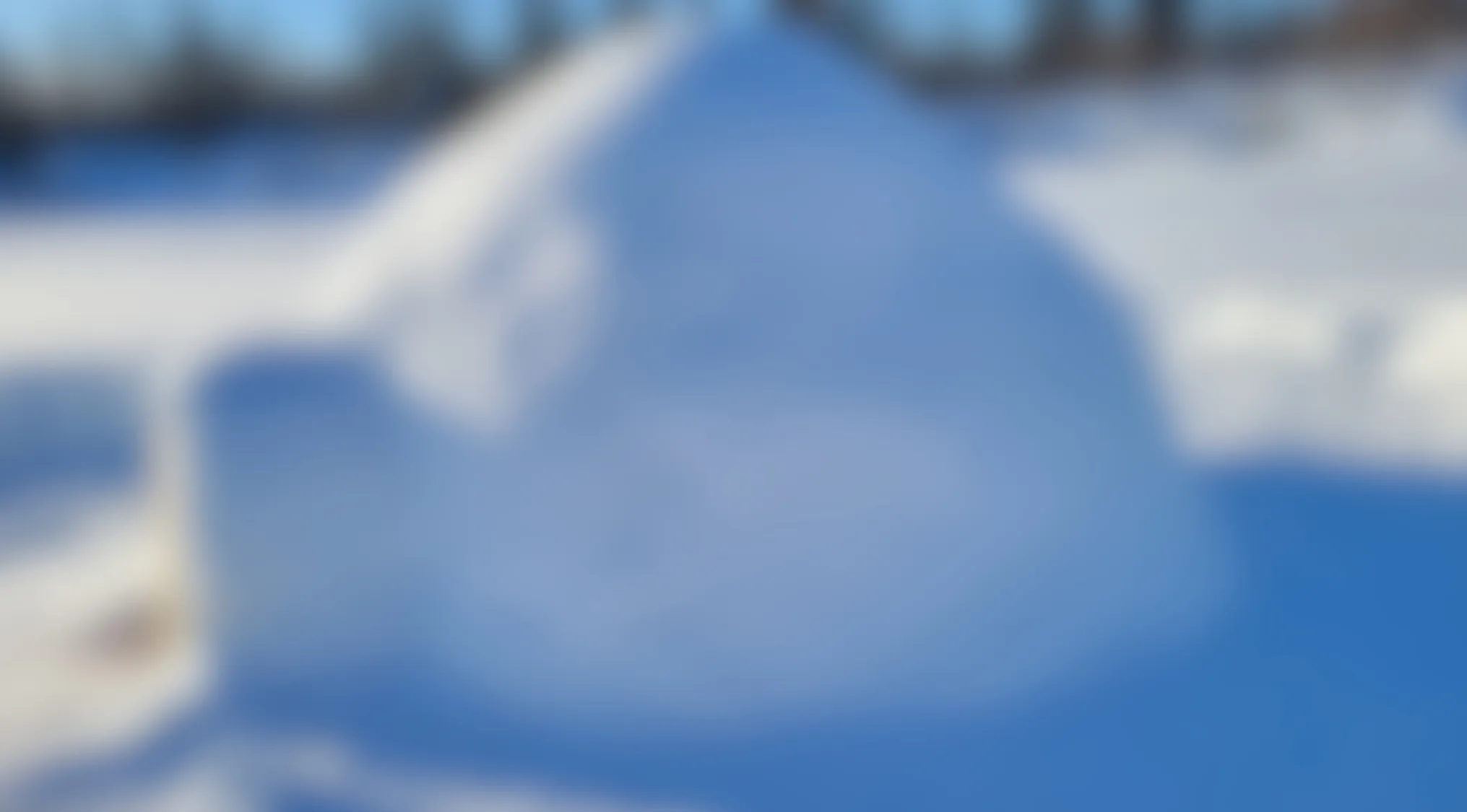 Blurry image of a large snow structure outdoors with bright blue sky and snow-covered ground in the background