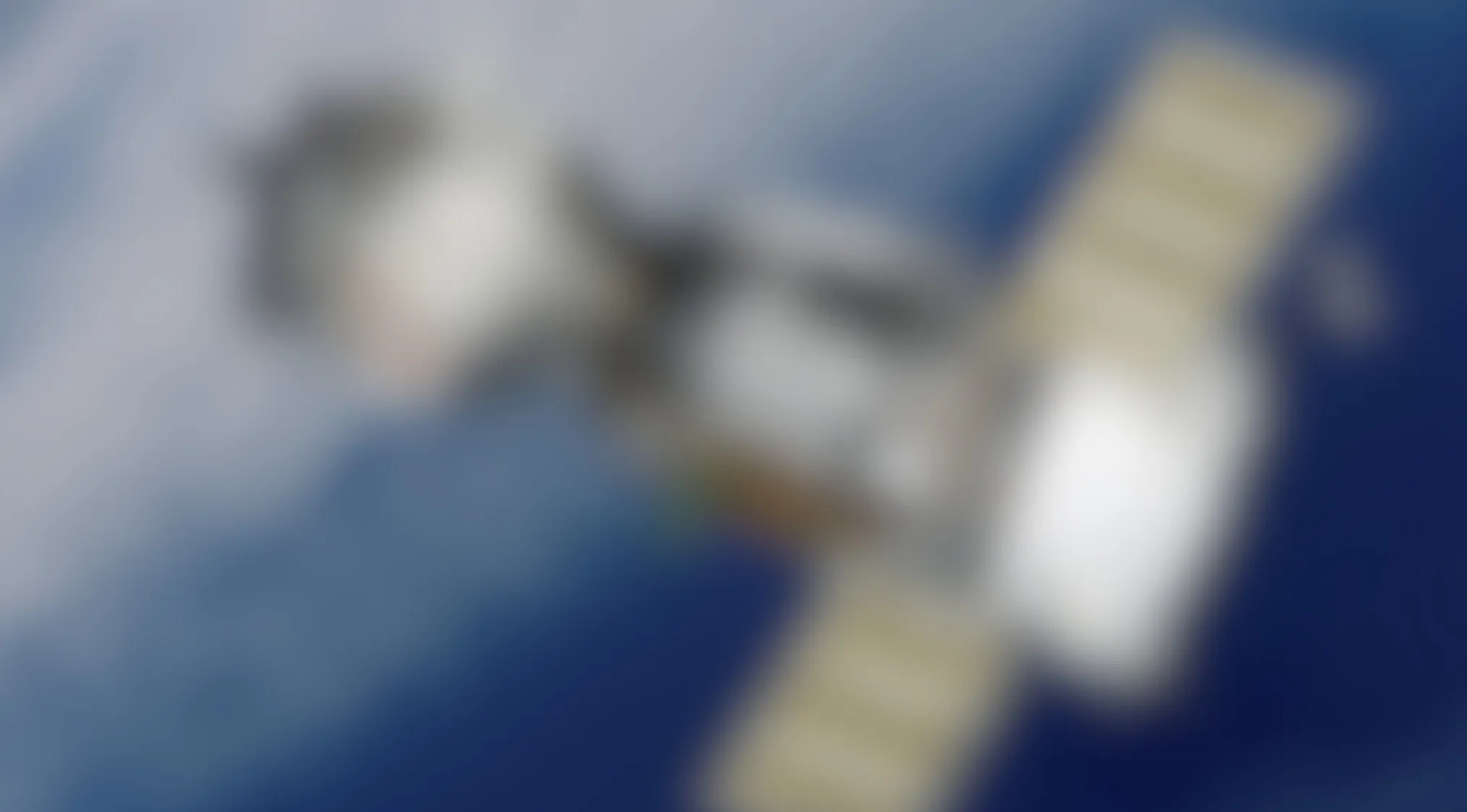 Blurry image of a satellite orbiting Earth with solar panels extended against a blue background.