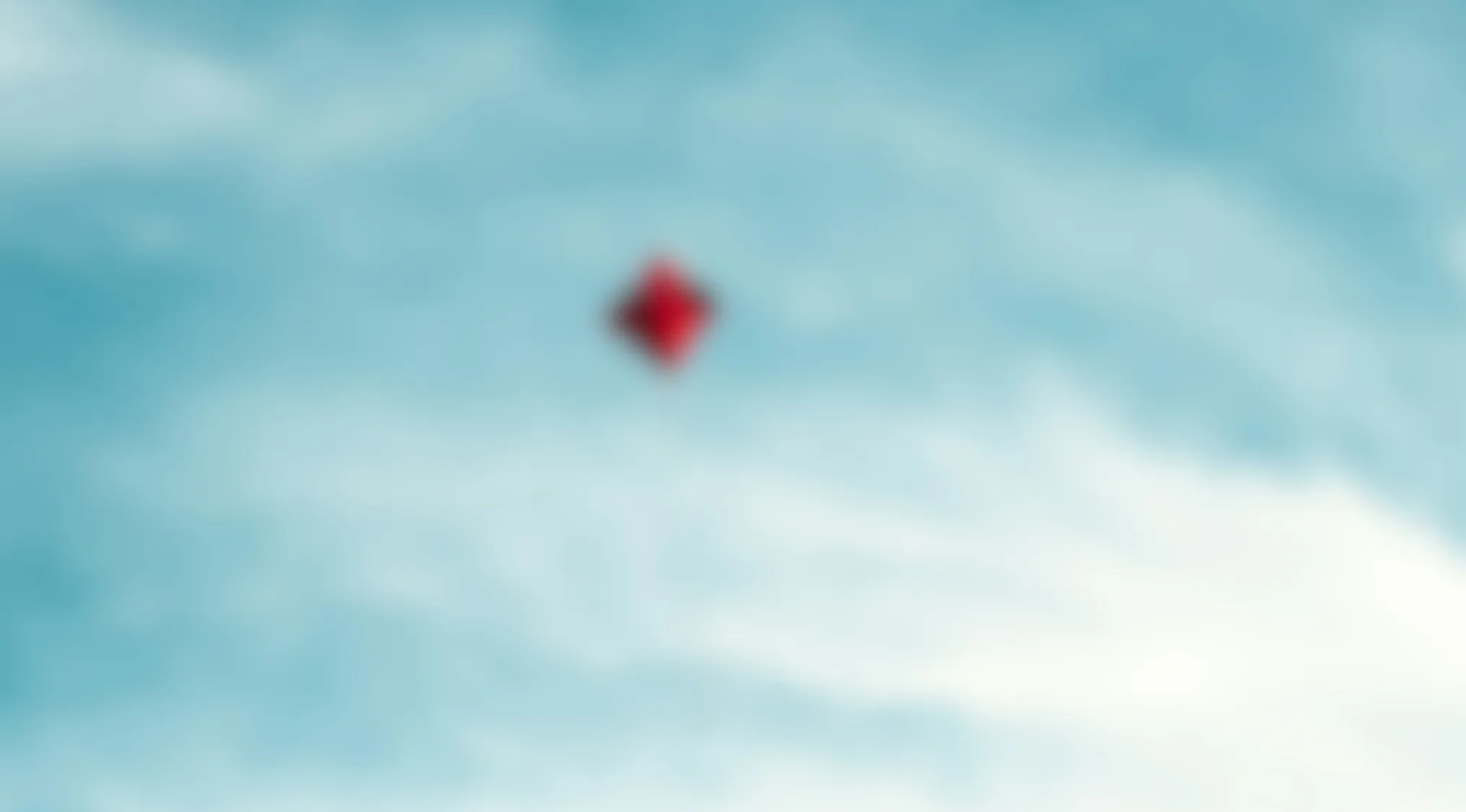 Blurry image of a red kite flying against a blue sky with light clouds in the background