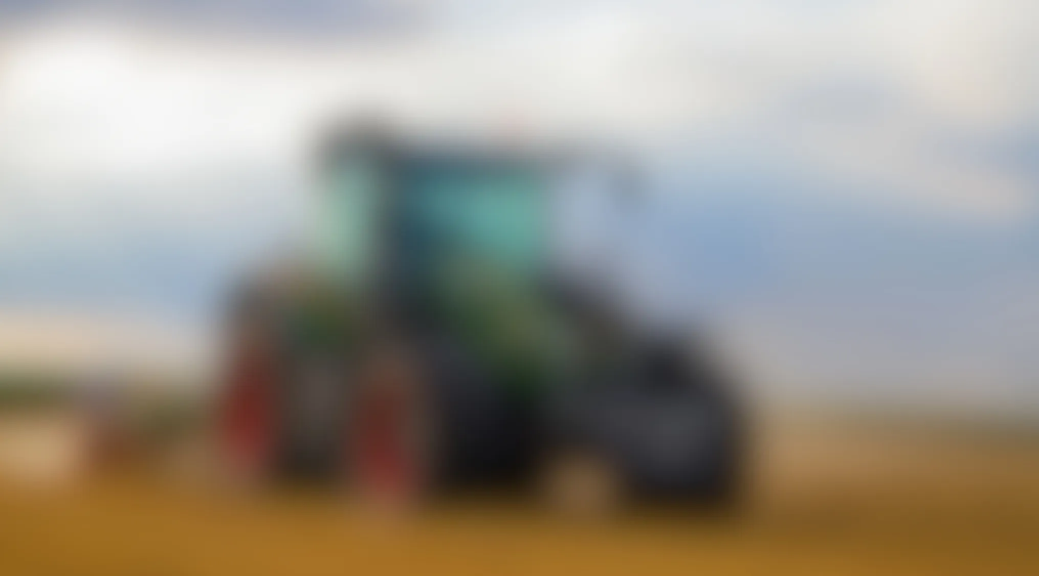Blurry image of a large green and black vehicle with red wheels in an open field under a cloudy sky