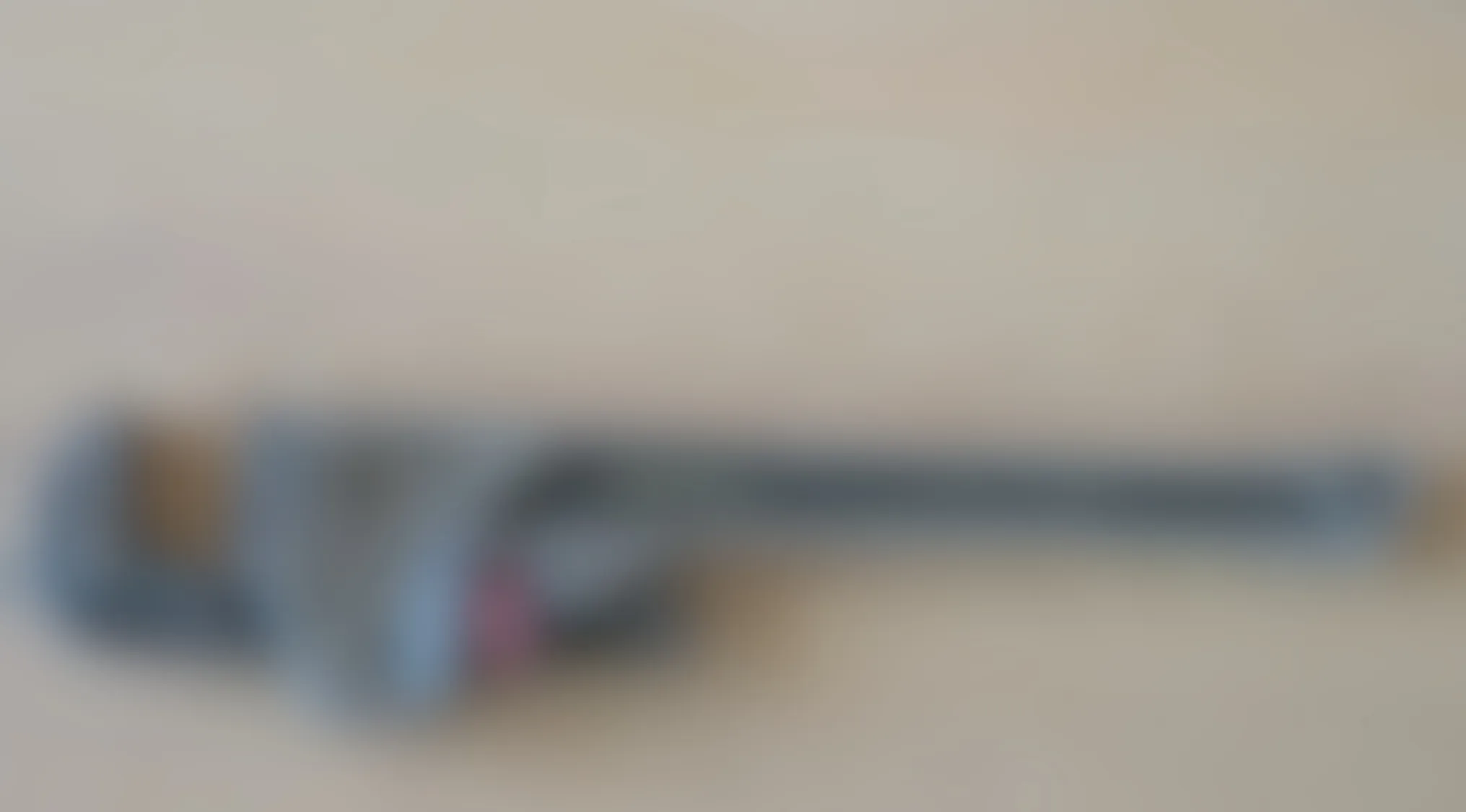Blurry image of an adjustable pipe wrench lying flat on a light surface, showing the tool shape and handle.