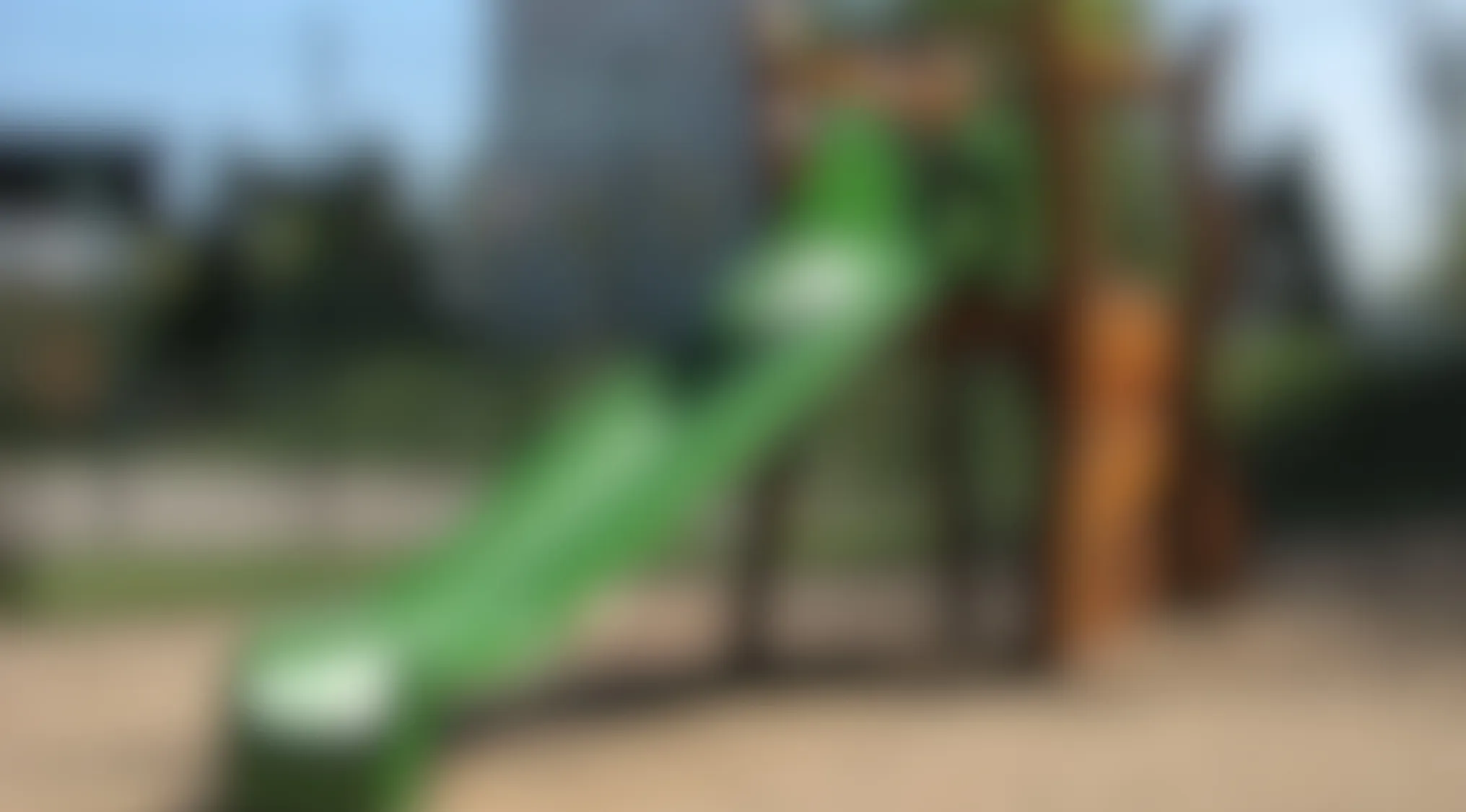 Blurry image of a green playground slide and wooden play structure on a sunny day outdoors.
