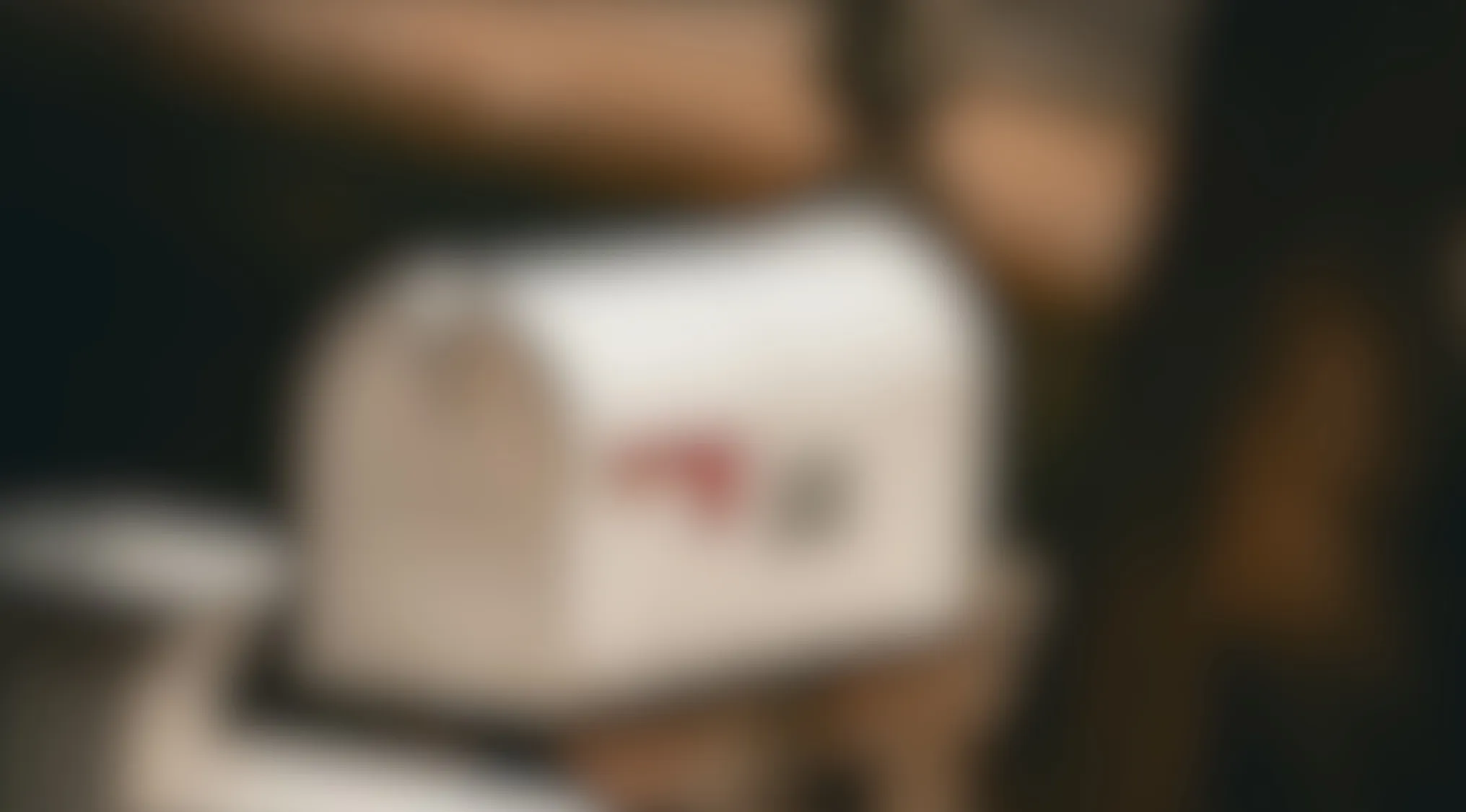 Blurry image showing a common object with a white mailbox shape and red flag on a wooden post background.