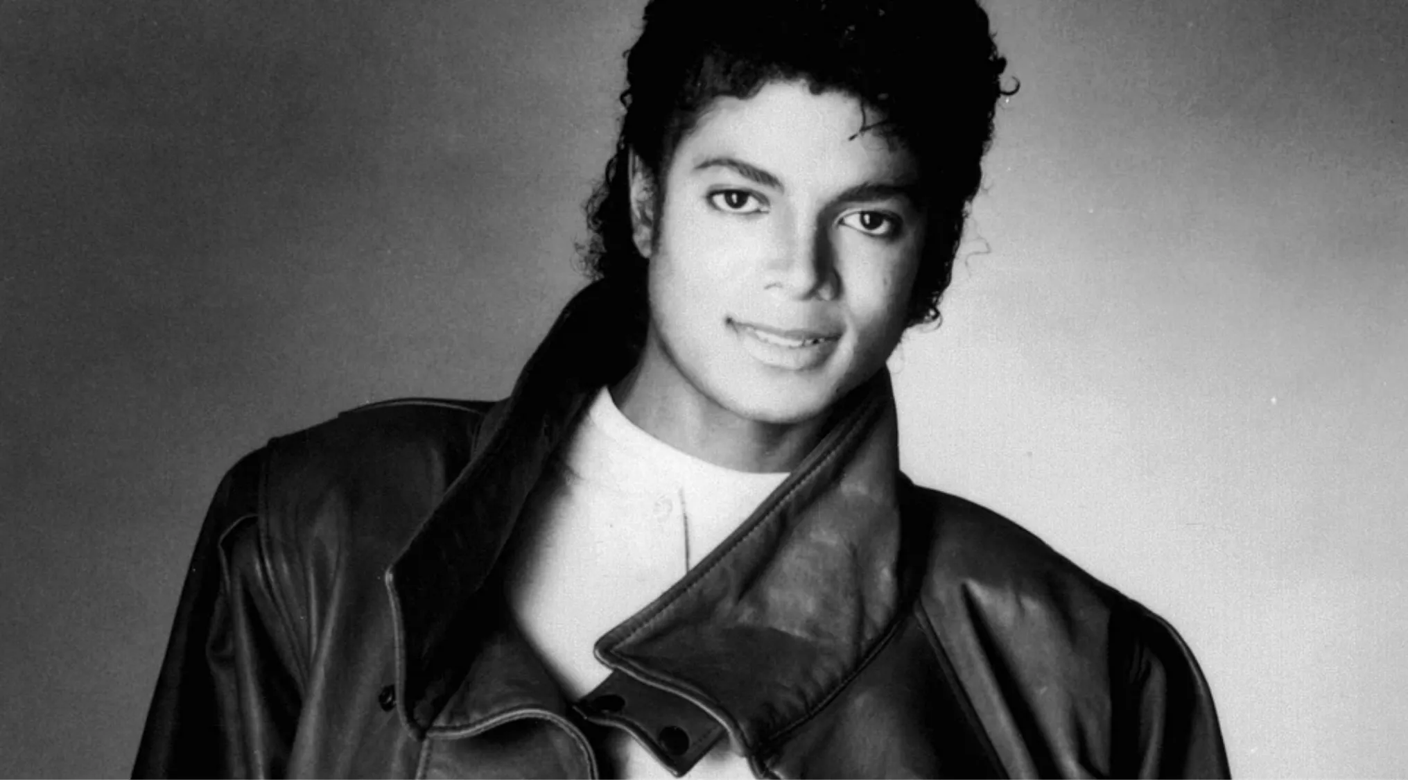 Black and white portrait of a famous person wearing a leather jacket and smiling, part of famous people identification.