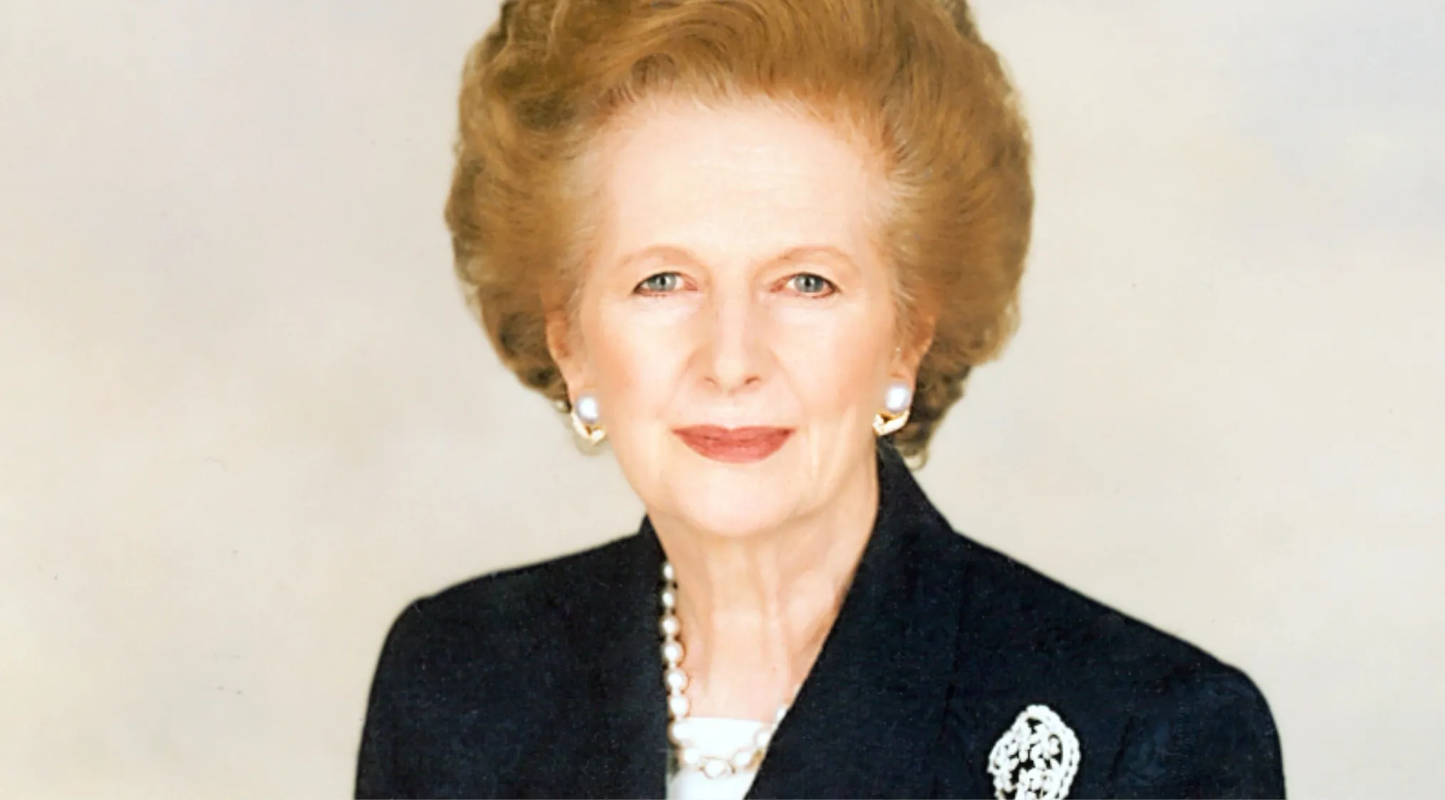 Portrait of British prime minister known as the Iron Lady, wearing pearl earrings and a black suit jacket.