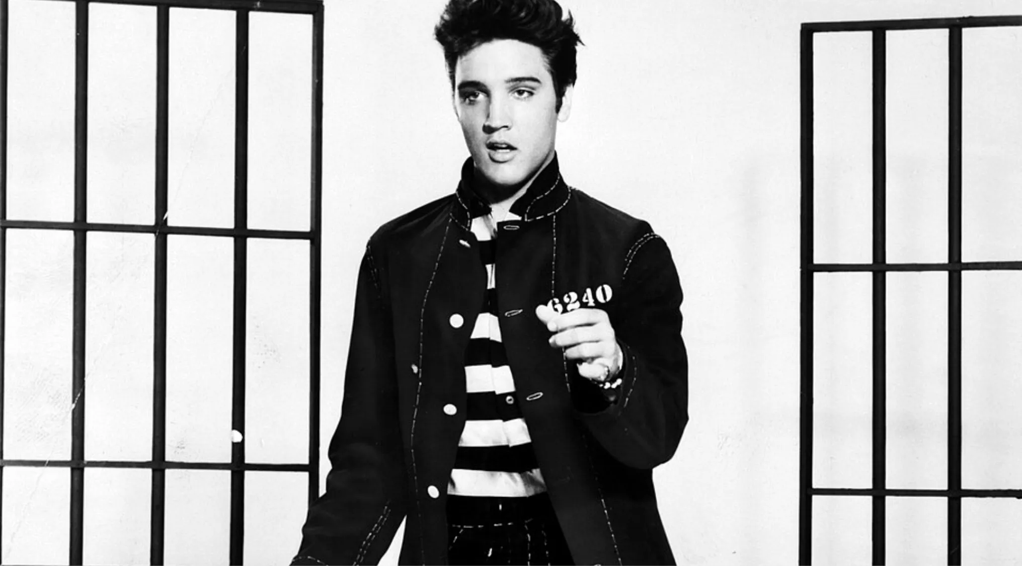 Black and white photo of a famous person posing in a striped prison uniform with jail bars in the background.