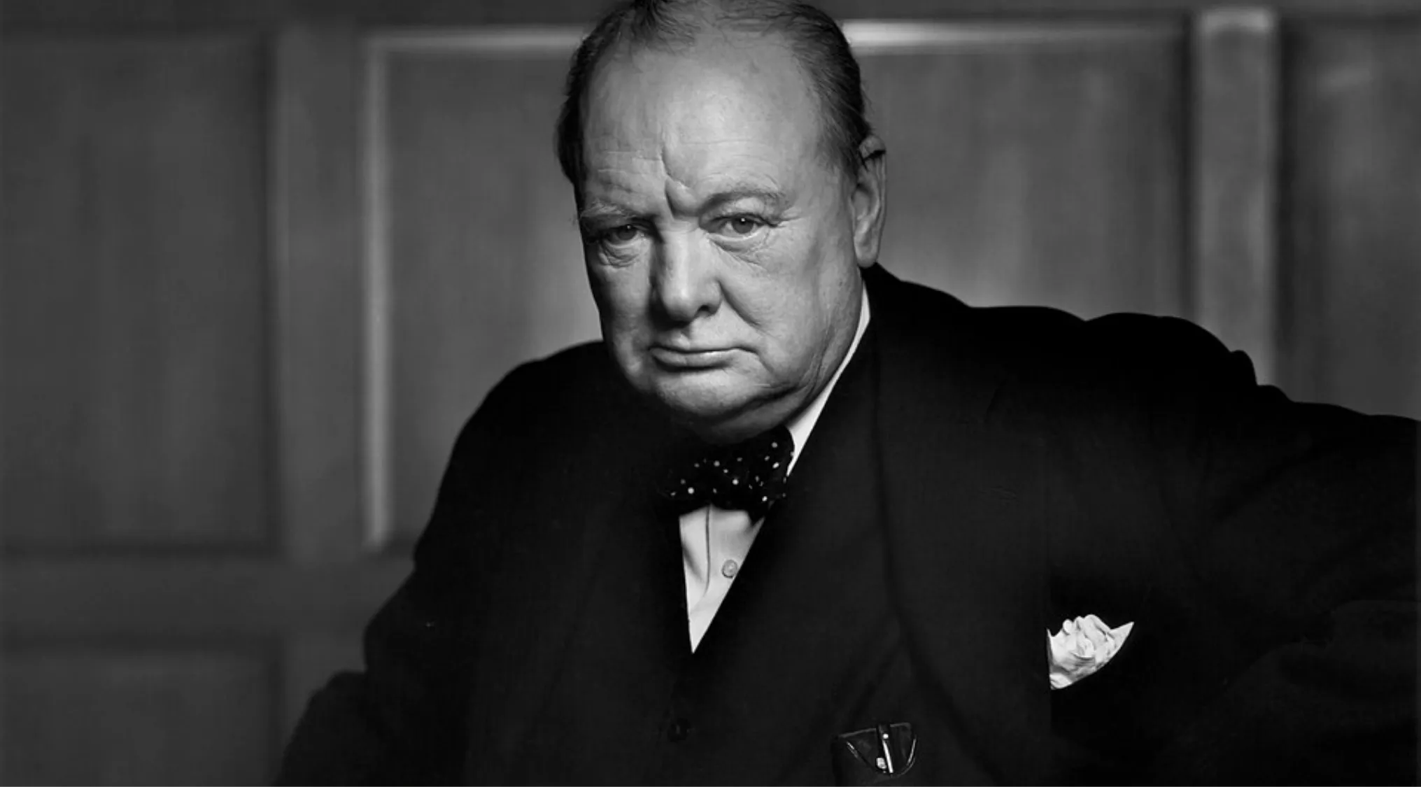 Black and white portrait of a famous person wearing a suit and bow tie, part of a famous people identification quiz.