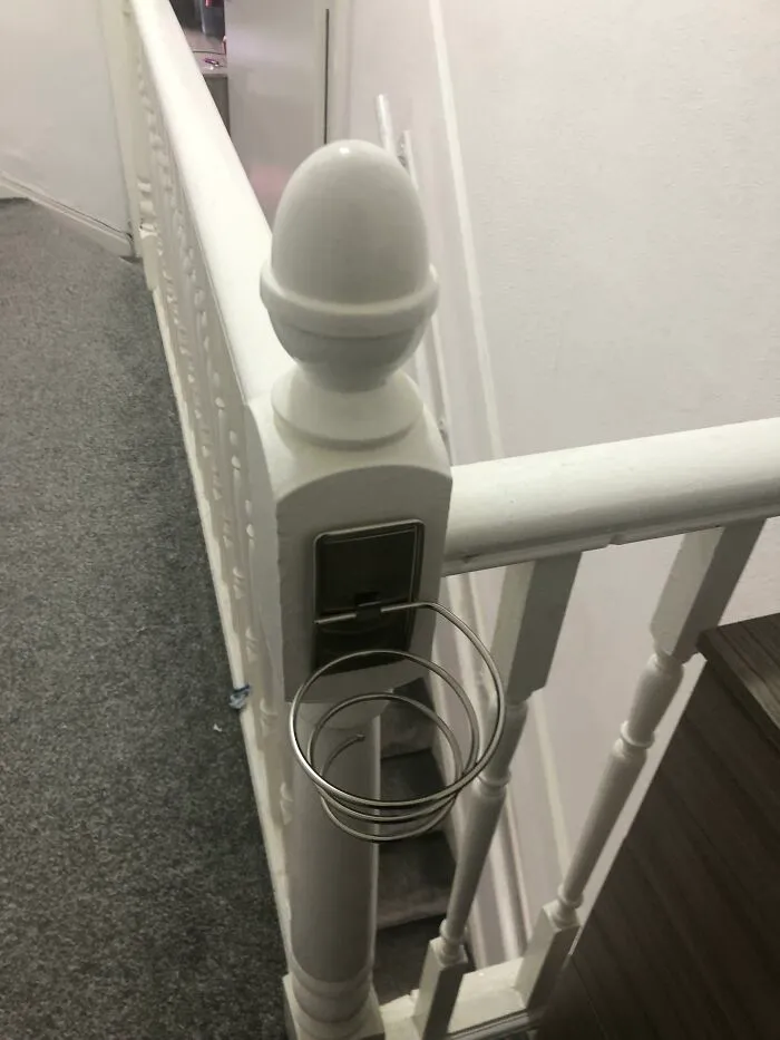Metal spiral cup holder attached to white stair railing, an example of internet solving mystery of unidentified objects.