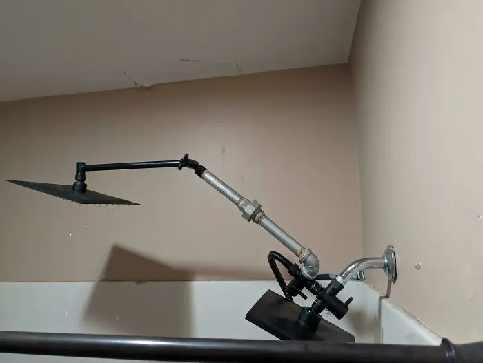 Improvised redneck engineering shower setup with mismatched pipes and showerheads mounted in a bathtub corner.