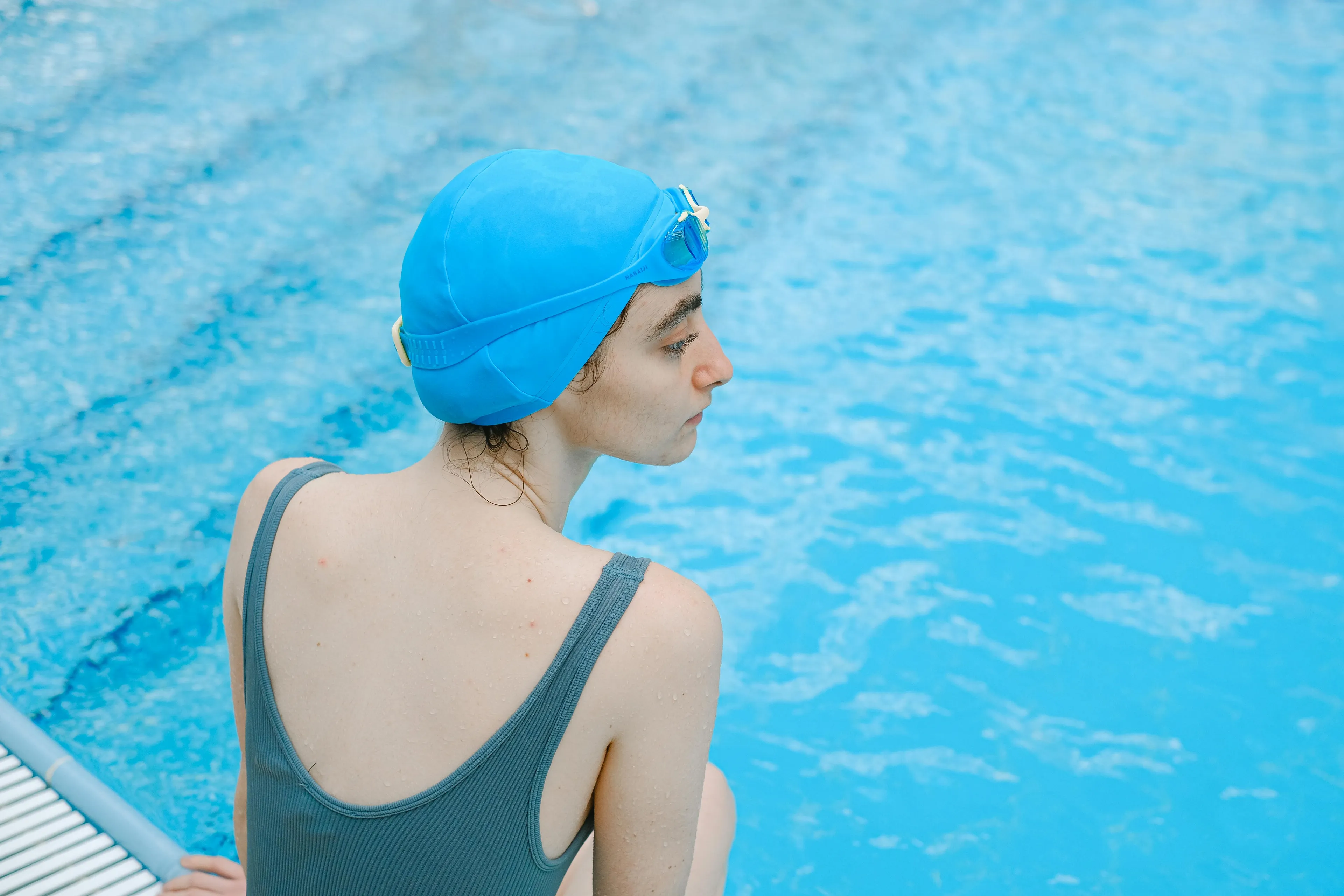 Woman in a blue swim cap sitting by the pool, illustrating science general knowledge about feeling colder on a windy day.