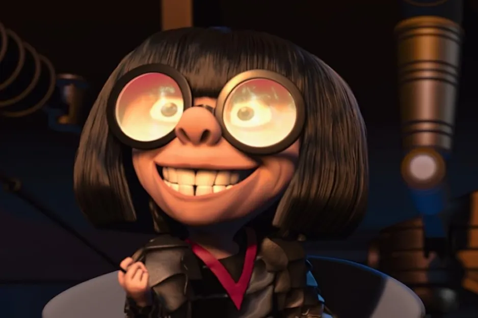 Edna Mode from The Incredibles with round glasses and black bob hairstyle smiling in a dark room setting.