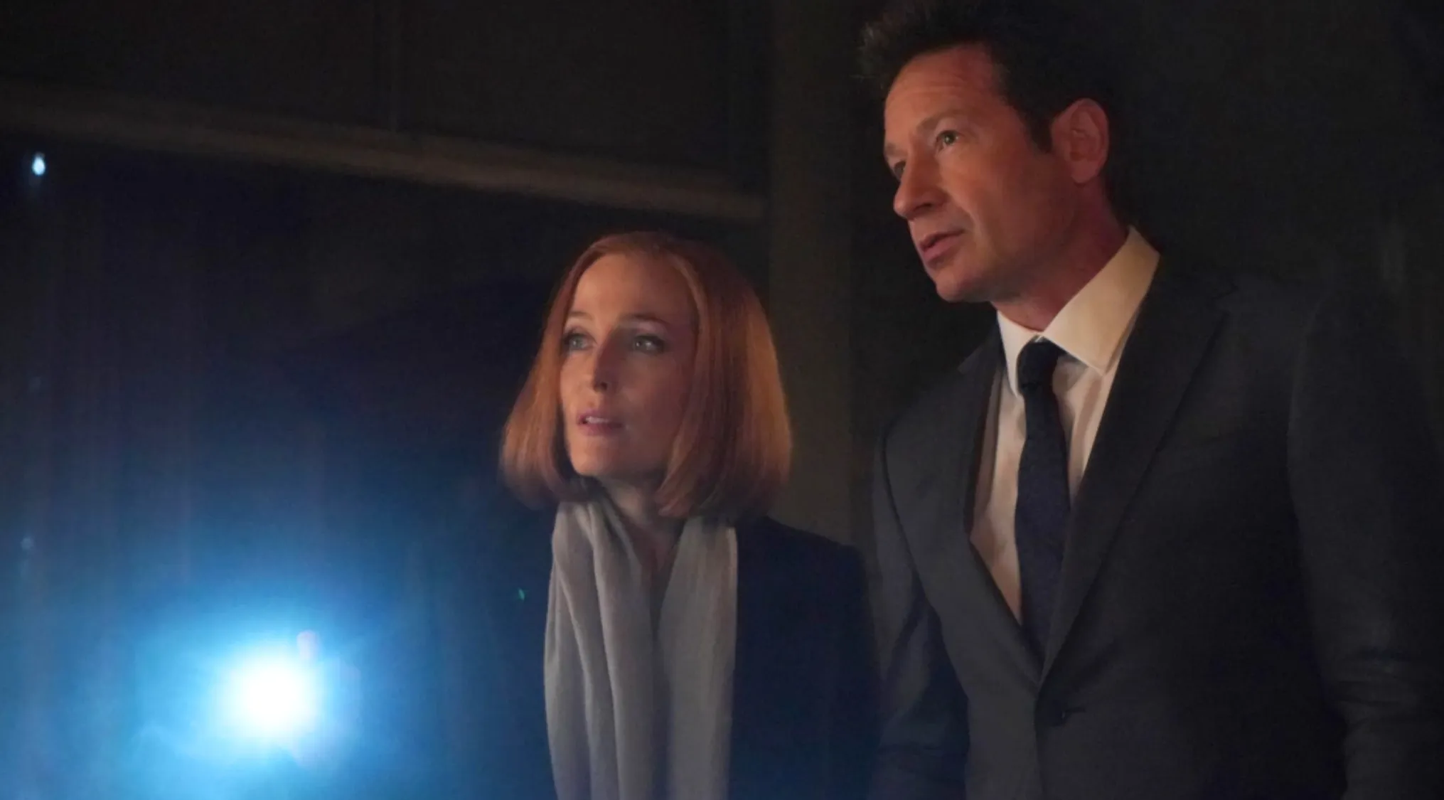 Fox Mulder and Dana Scully from The X-Files investigating with a flashlight in a dark setting.