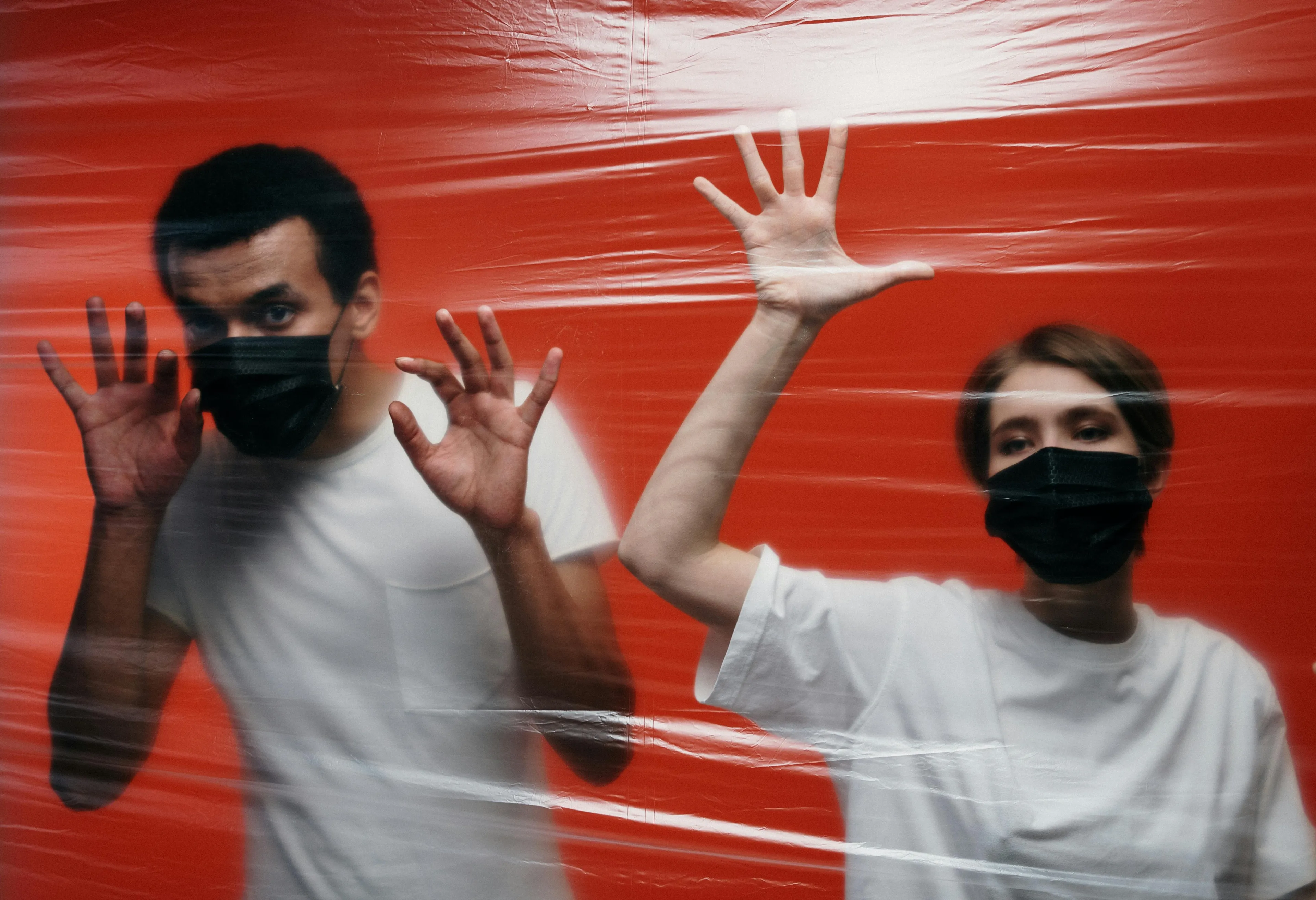 Two people wearing masks behind plastic film, illustrating science general knowledge about virus exposure and symptoms difference.