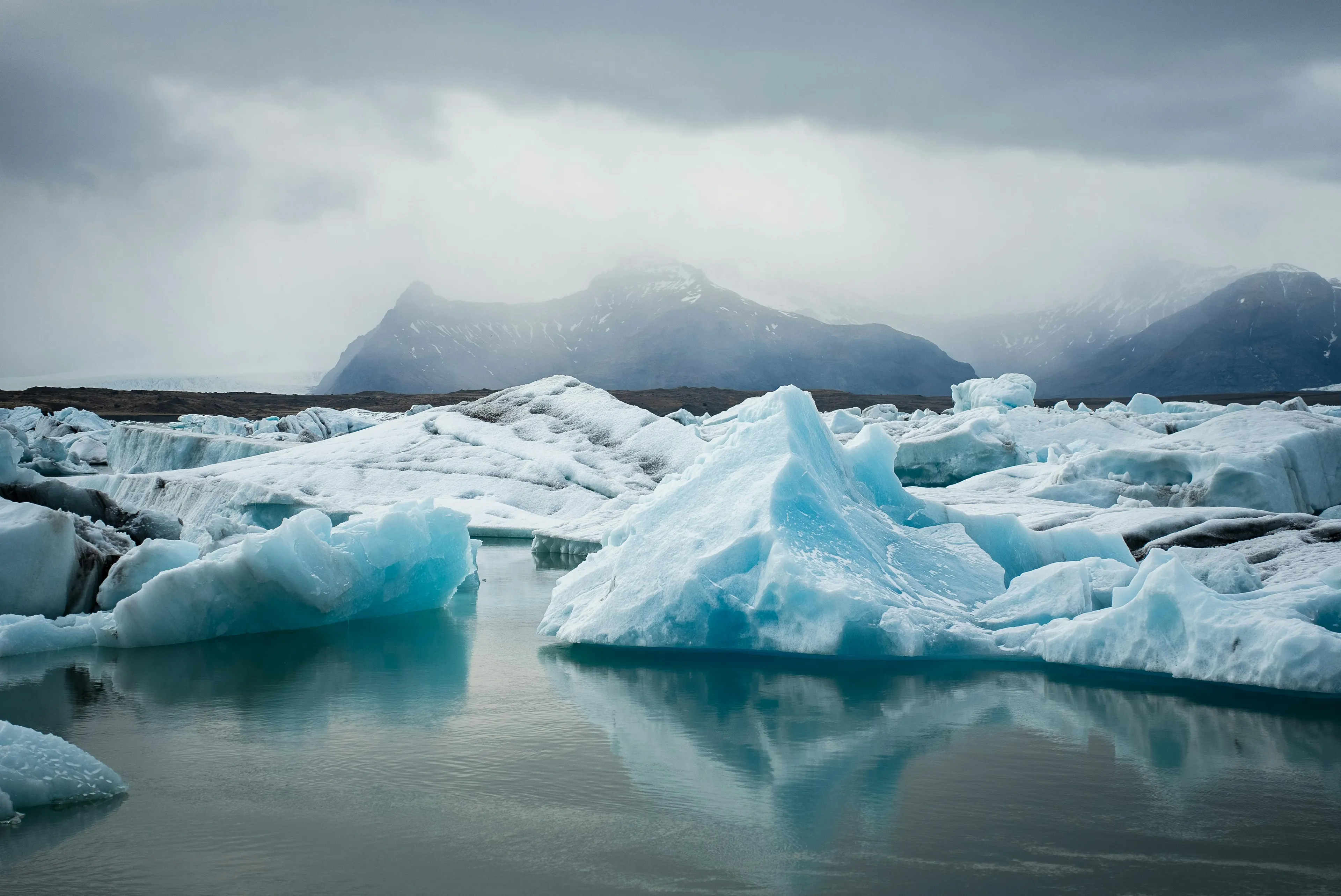 Melting glacier with ice floating in cold water and mountains shrouded in mist in the surrounding area.