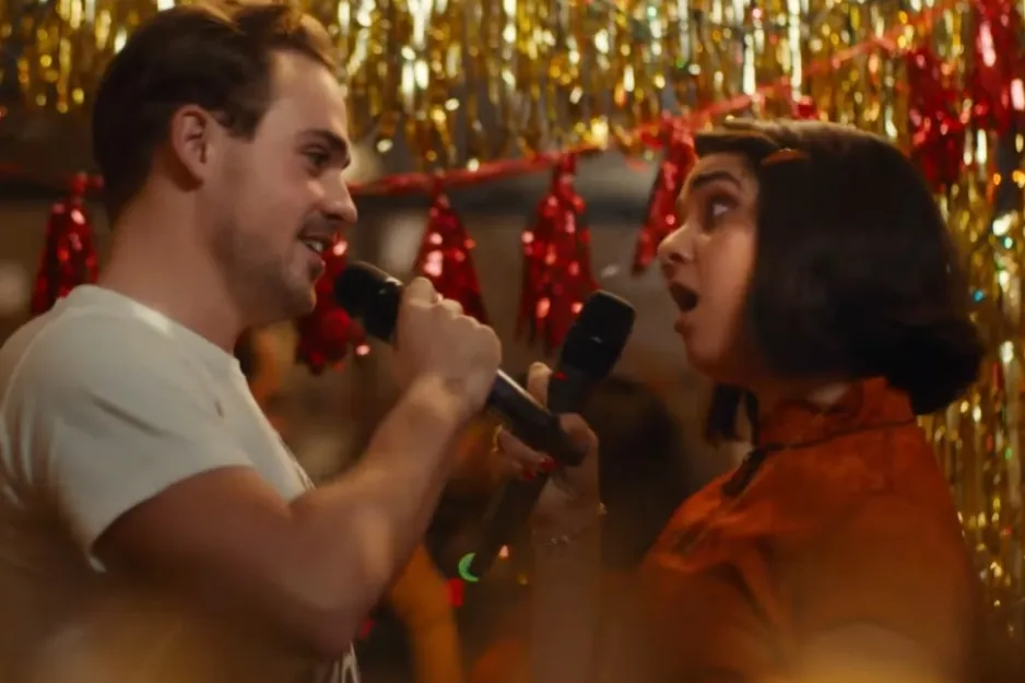 Man and woman singing with microphones at a festive party, decorated with gold and red streamers, Harry and Sally image.