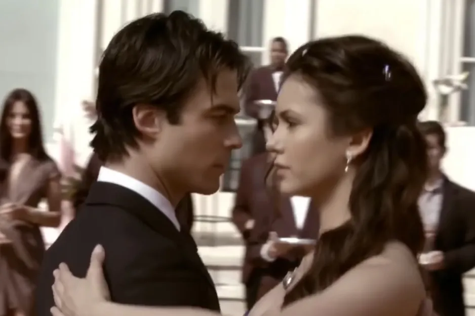 Couple from The Vampire Diaries dancing closely at a formal event with blurred guests in the background.