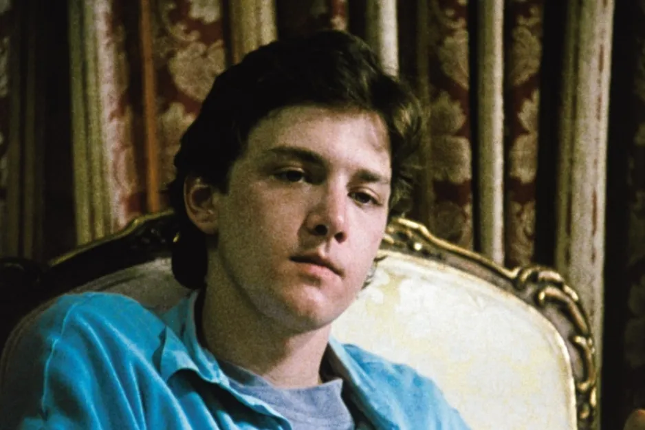 Young man from Pretty in Pink movie sitting on an ornate chair, reflecting on who Andie ends up with in the story.