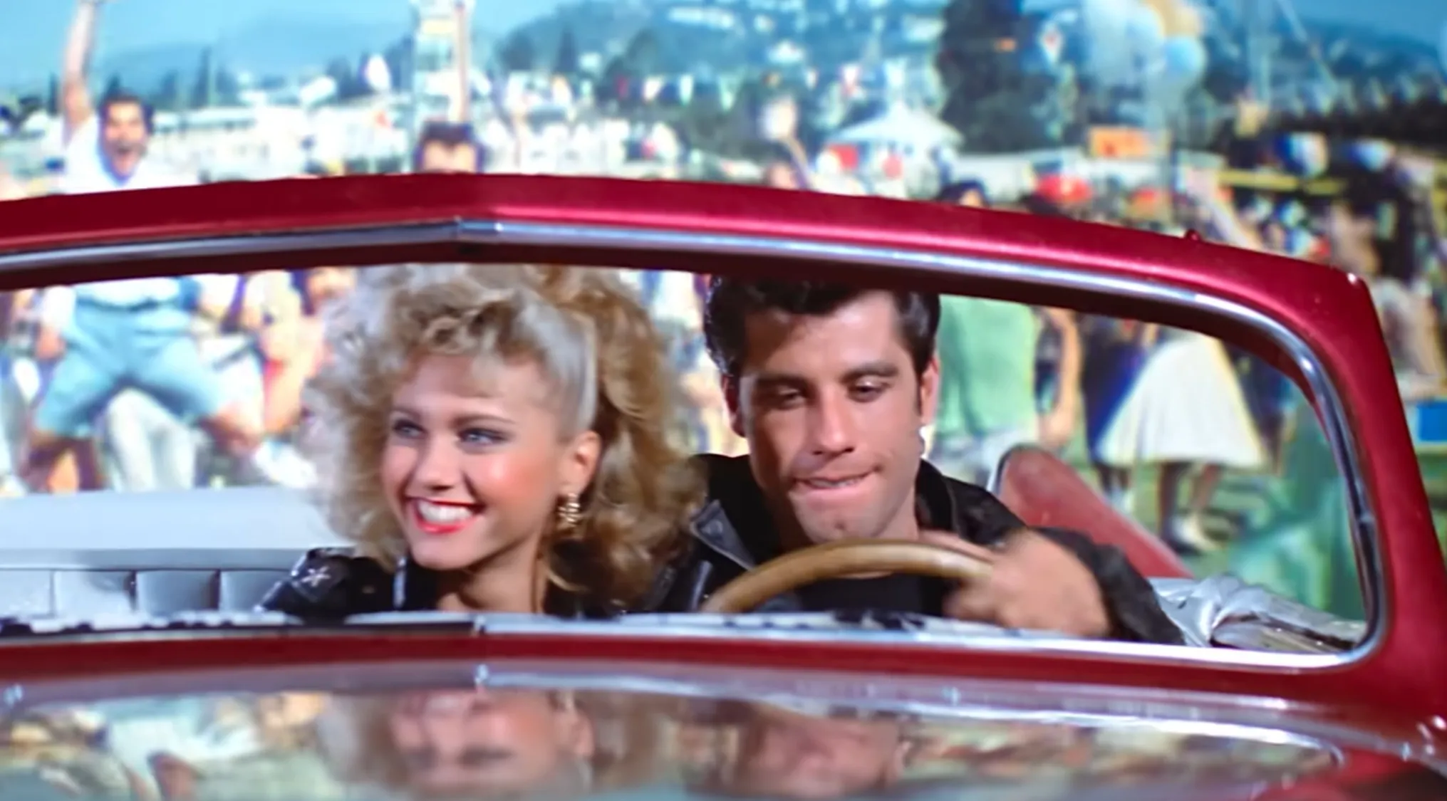 Couple in a red car smiling and driving, featured in a fictional couples quiz from a musical scene.