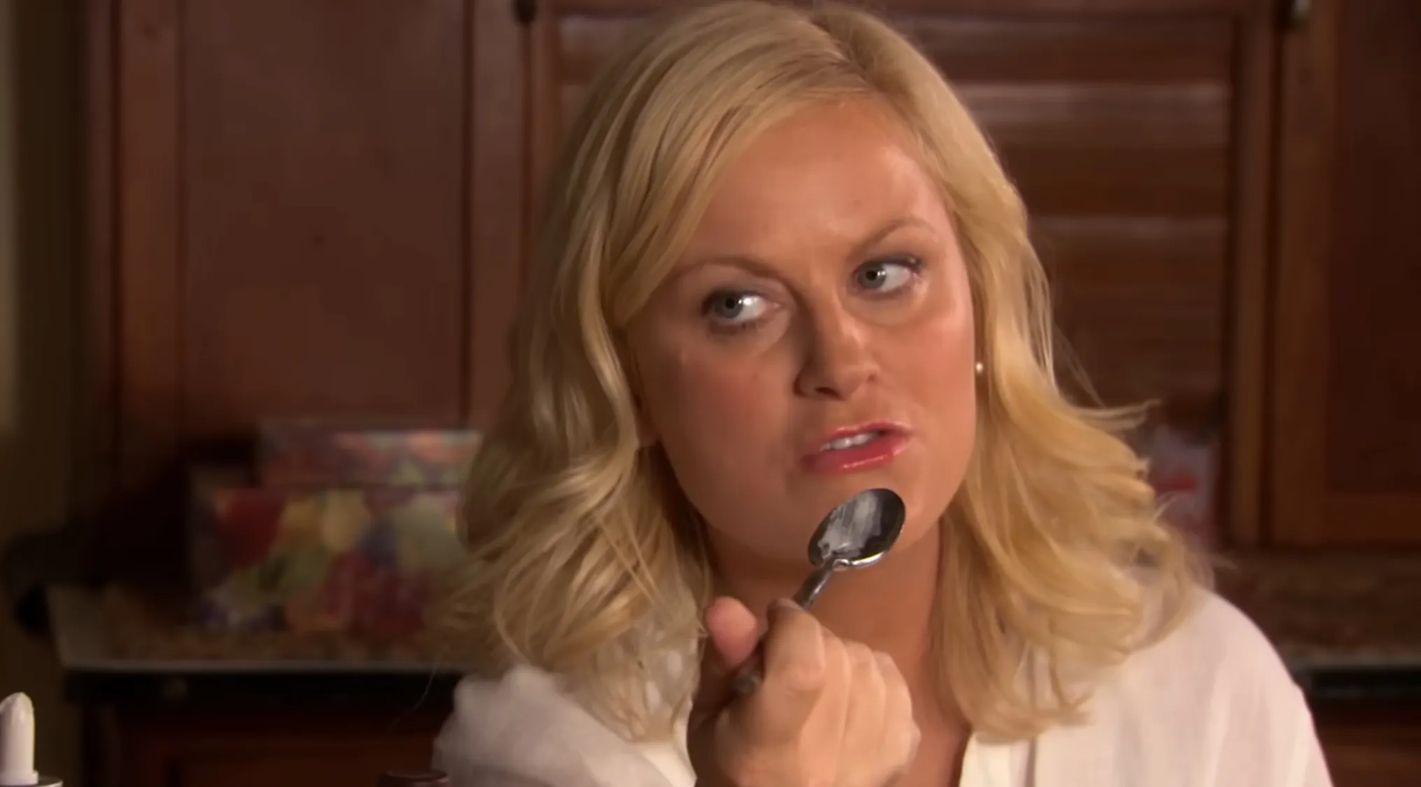 Leslie Knope from Parks and Recreation holding a spoon near her mouth, looking thoughtfully to the side.