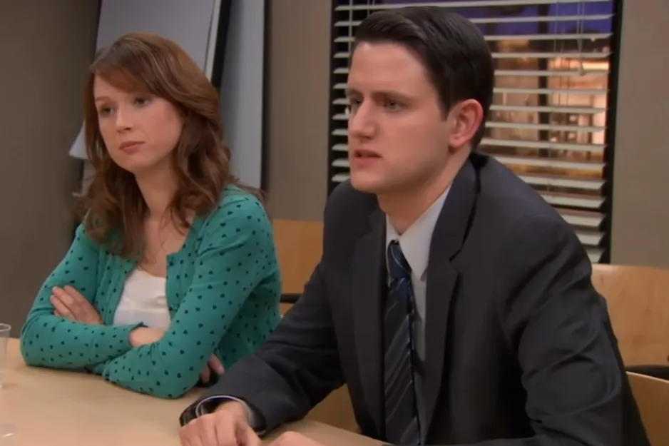 Couple from The Office TV show sitting at a table in an office setting with serious expressions during a meeting.