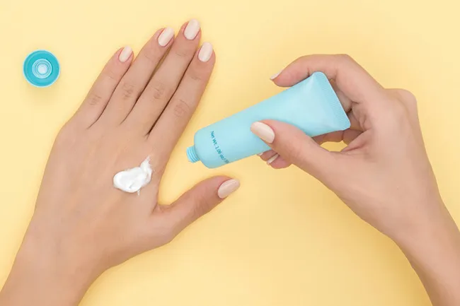 Hand cream being applied on the back of a hand with a small blue tube, perfect for carrying in your bag.