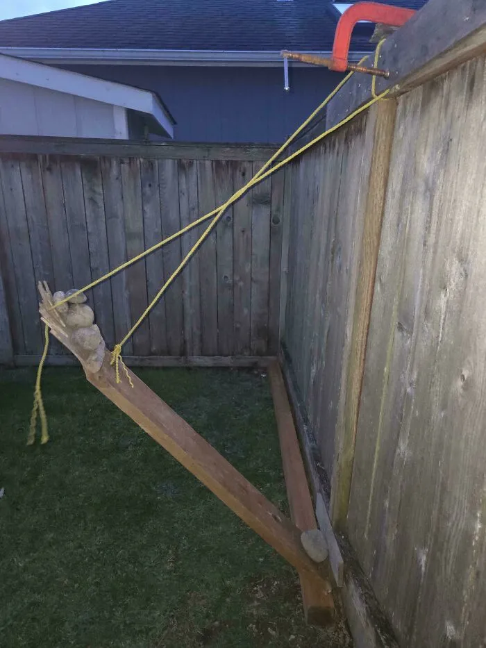 A makeshift fence repair using wooden beams, yellow rope, and a clamp as part of questionable DIY projects.