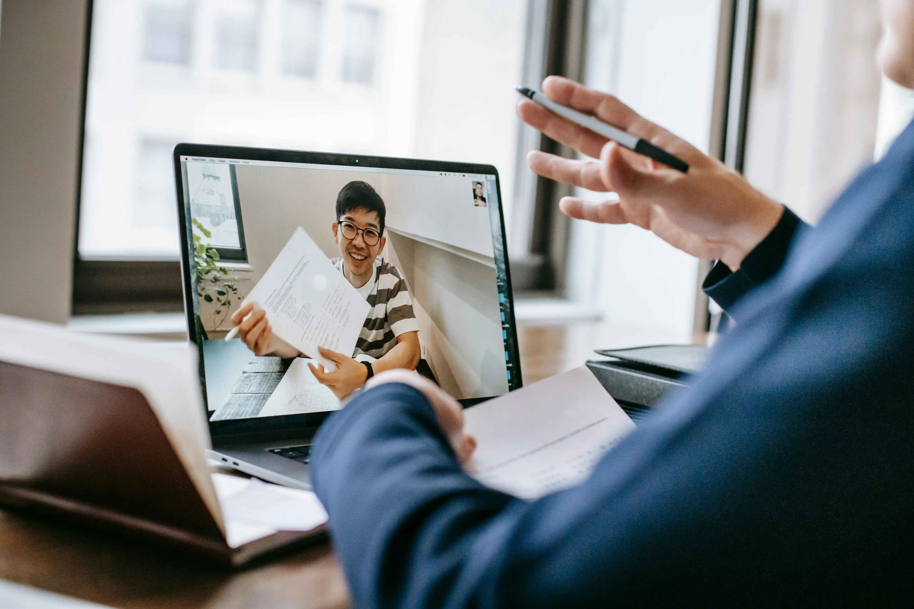 Person hosting a debate club online, interacting through video call while holding papers during a virtual meeting.