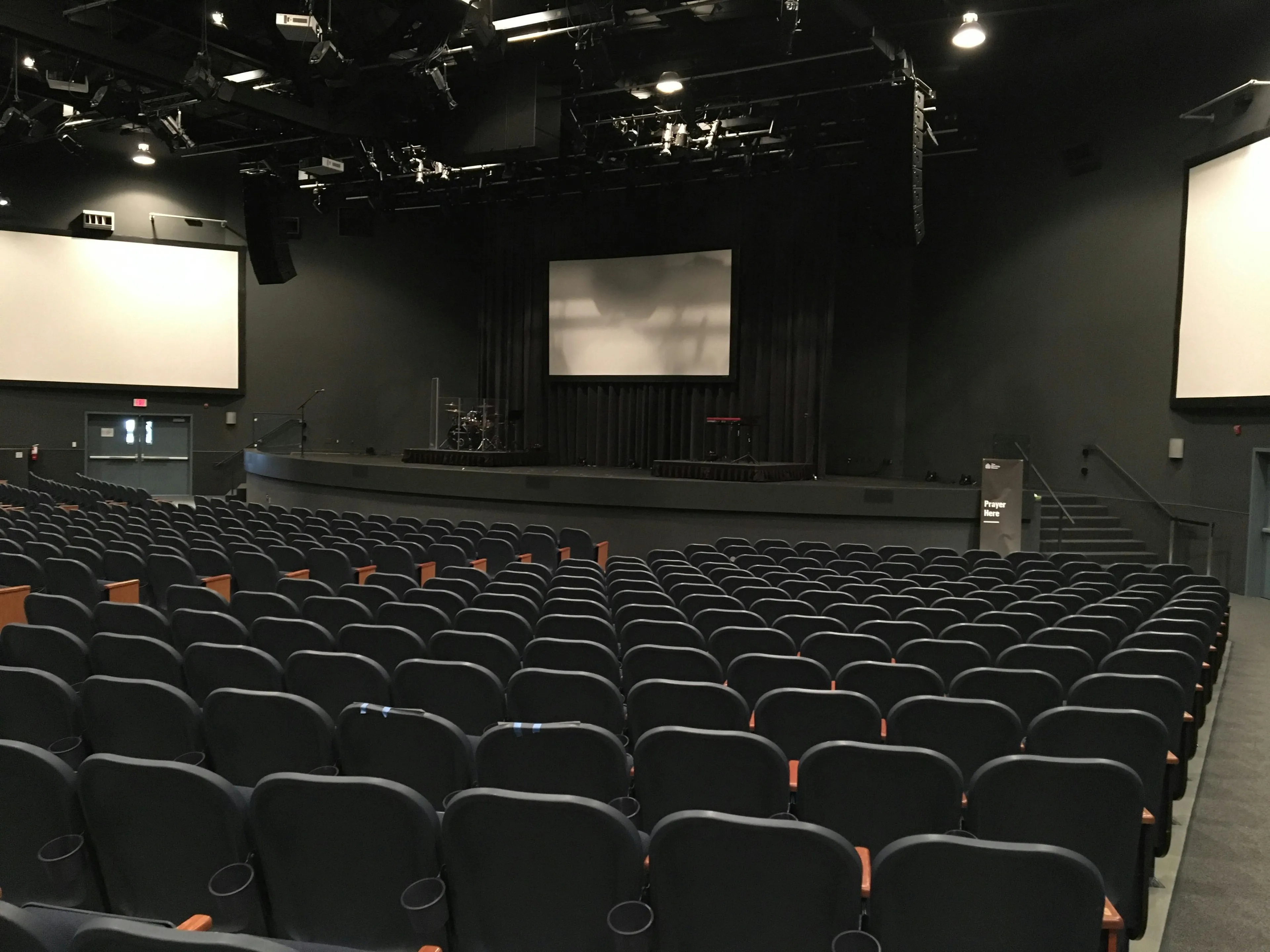 Large empty hall with rows of black chairs and a stage illustrating the cause of echo in science general knowledge.