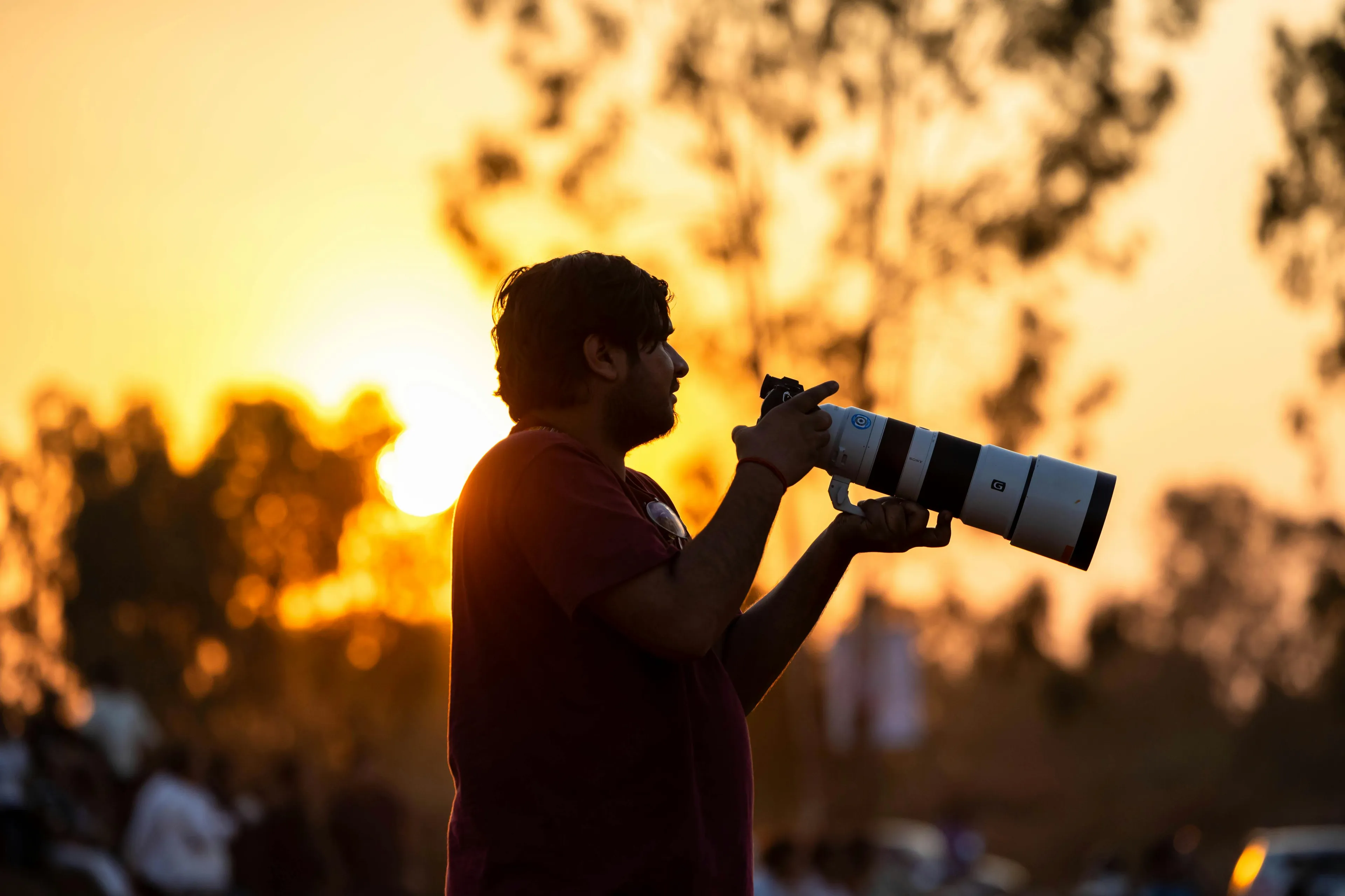 Photographer with telephoto lens capturing images during golden hour with warm sunlight and blurred nature background.