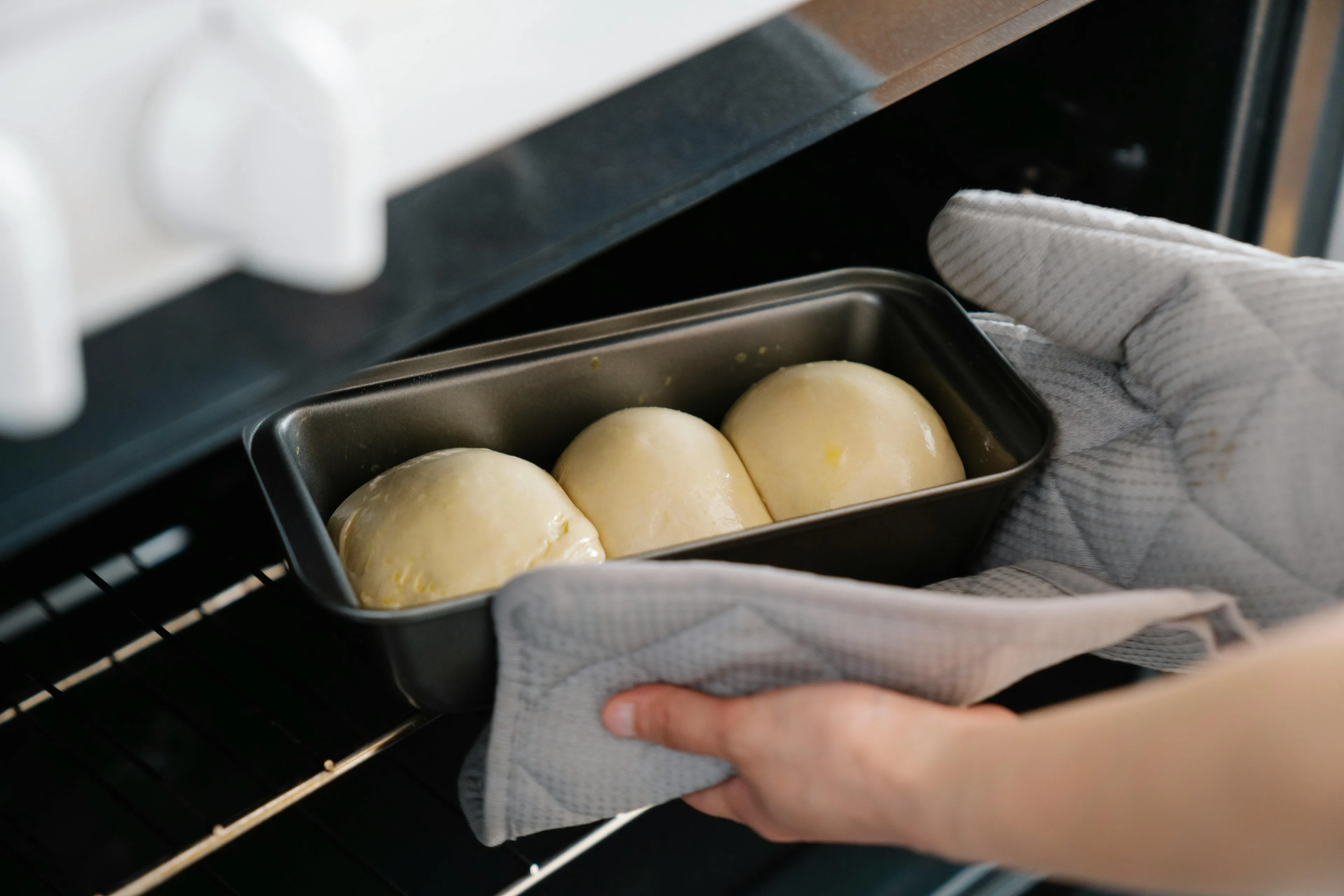 Hands with oven mitts placing yeast bread dough into an oven, illustrating carbon dioxide production in baking science.