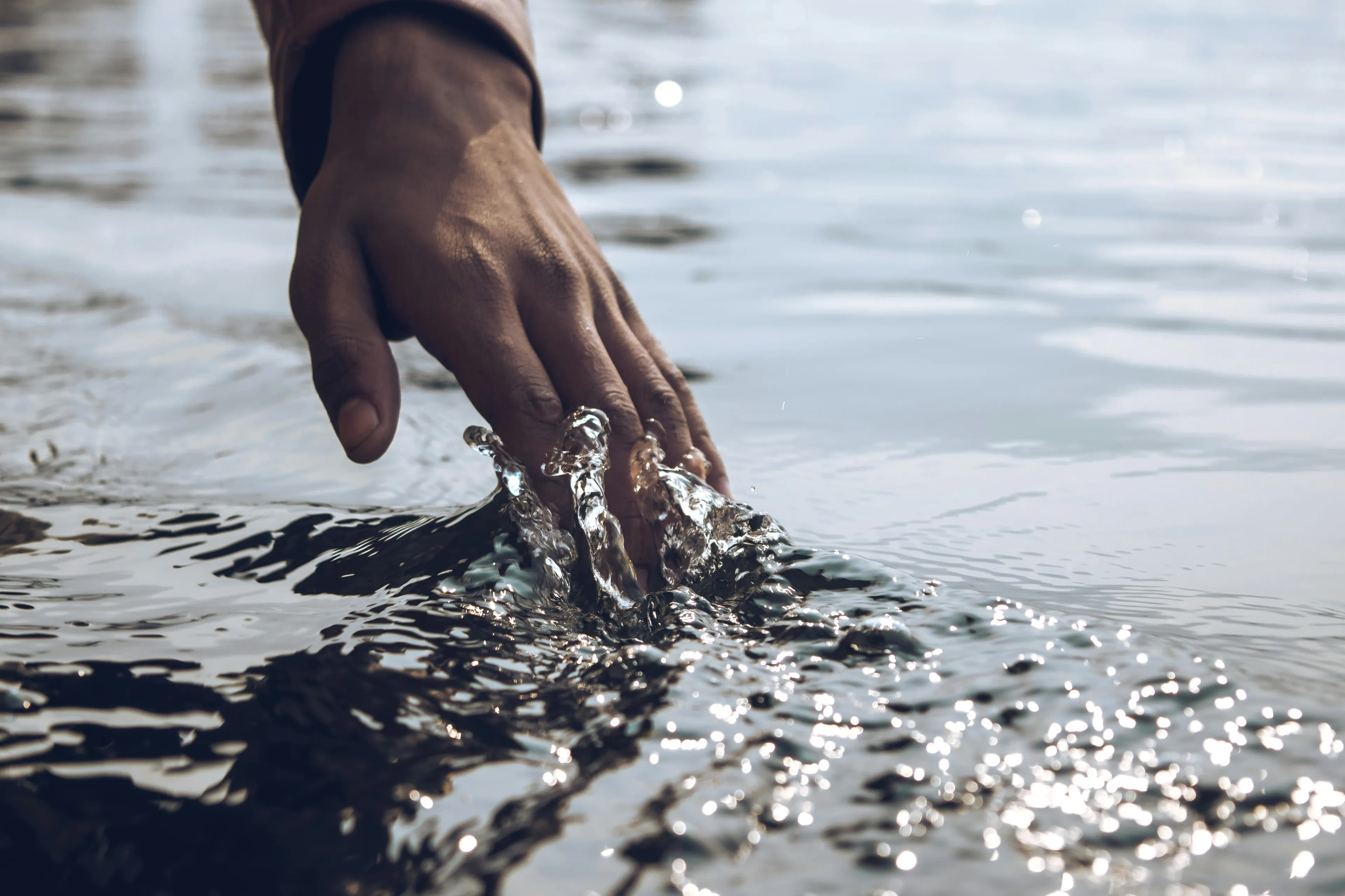 Hand touching water surface creating ripples illustrating resistance in water movement concept.