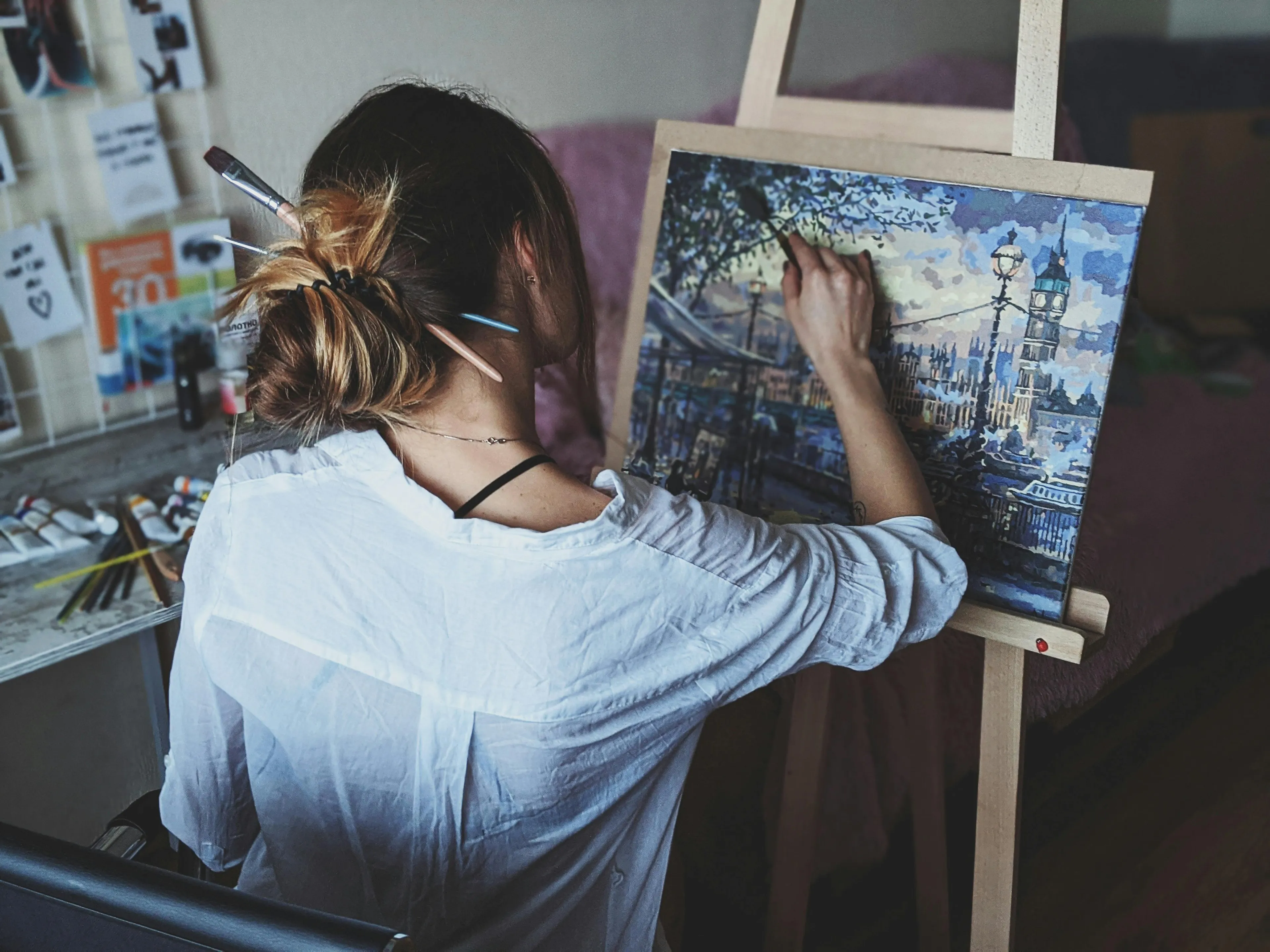 Artist painting a cityscape using perspective to make distant objects smaller, demonstrating scientific principle of depth.