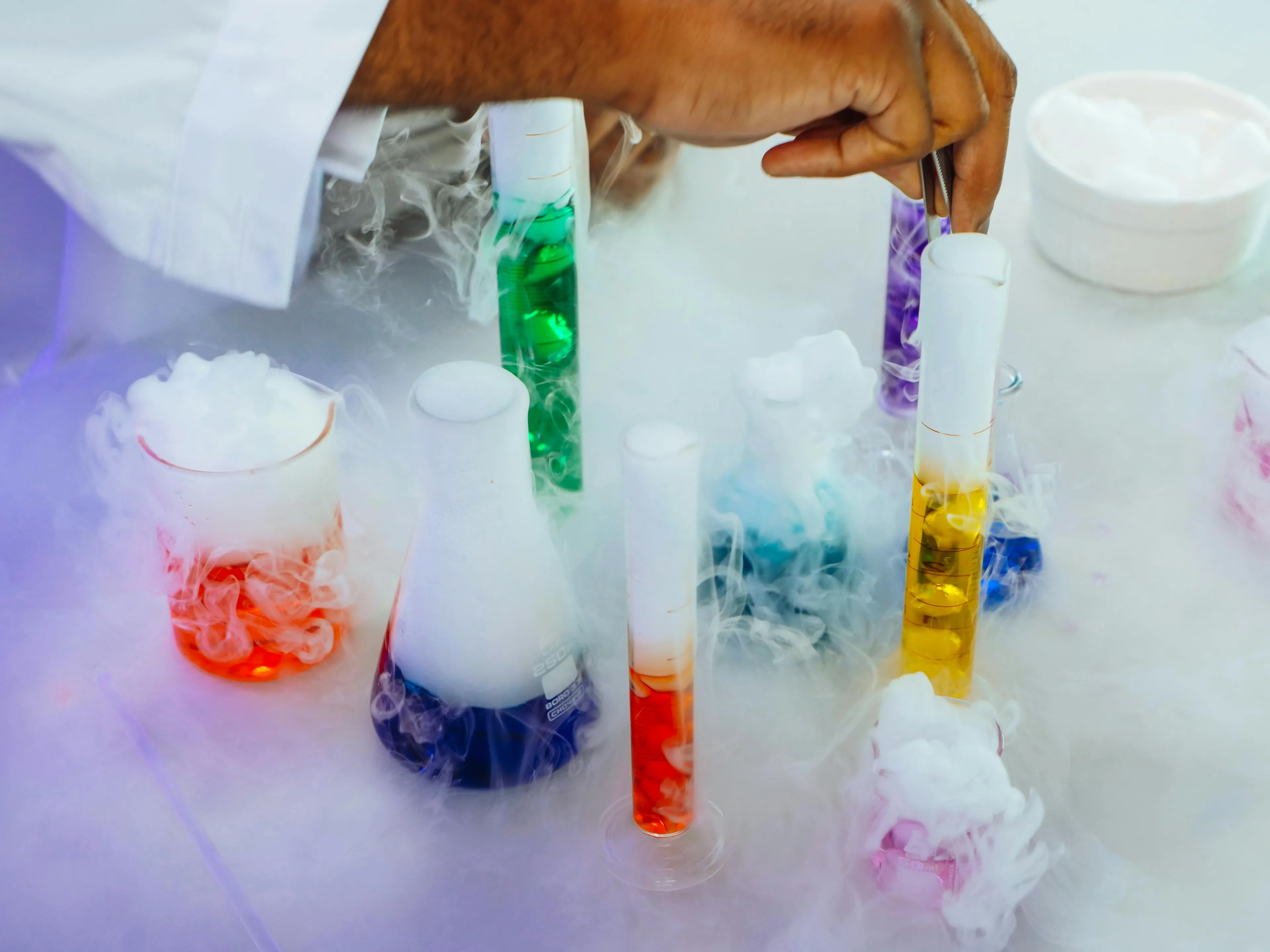 Scientist handling colorful chemical gases in test tubes with smoke, illustrating factors that increase chemical reaction rates.