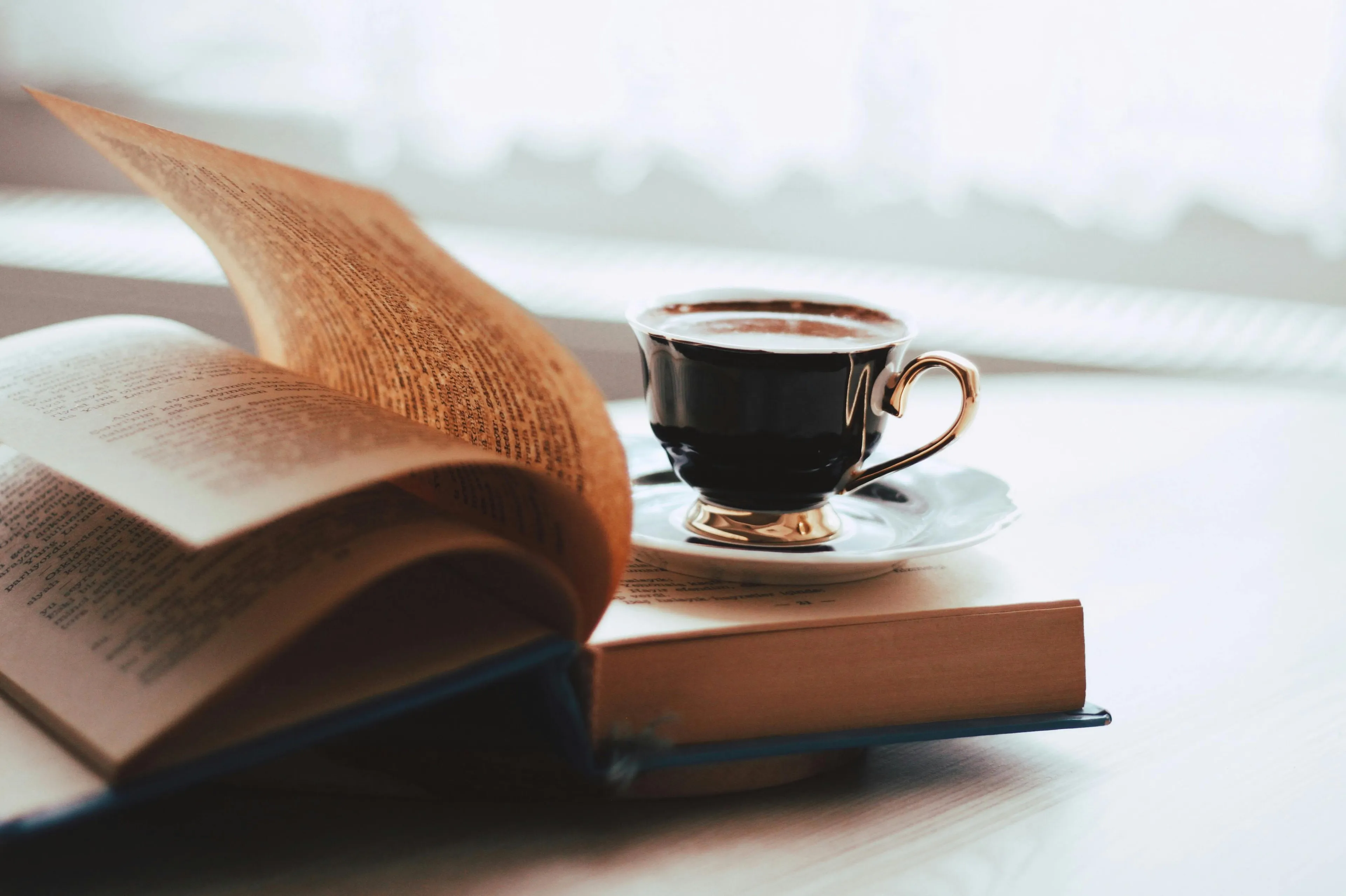Open book with flipping pages next to a black coffee cup on a white table, symbolizing science general knowledge.