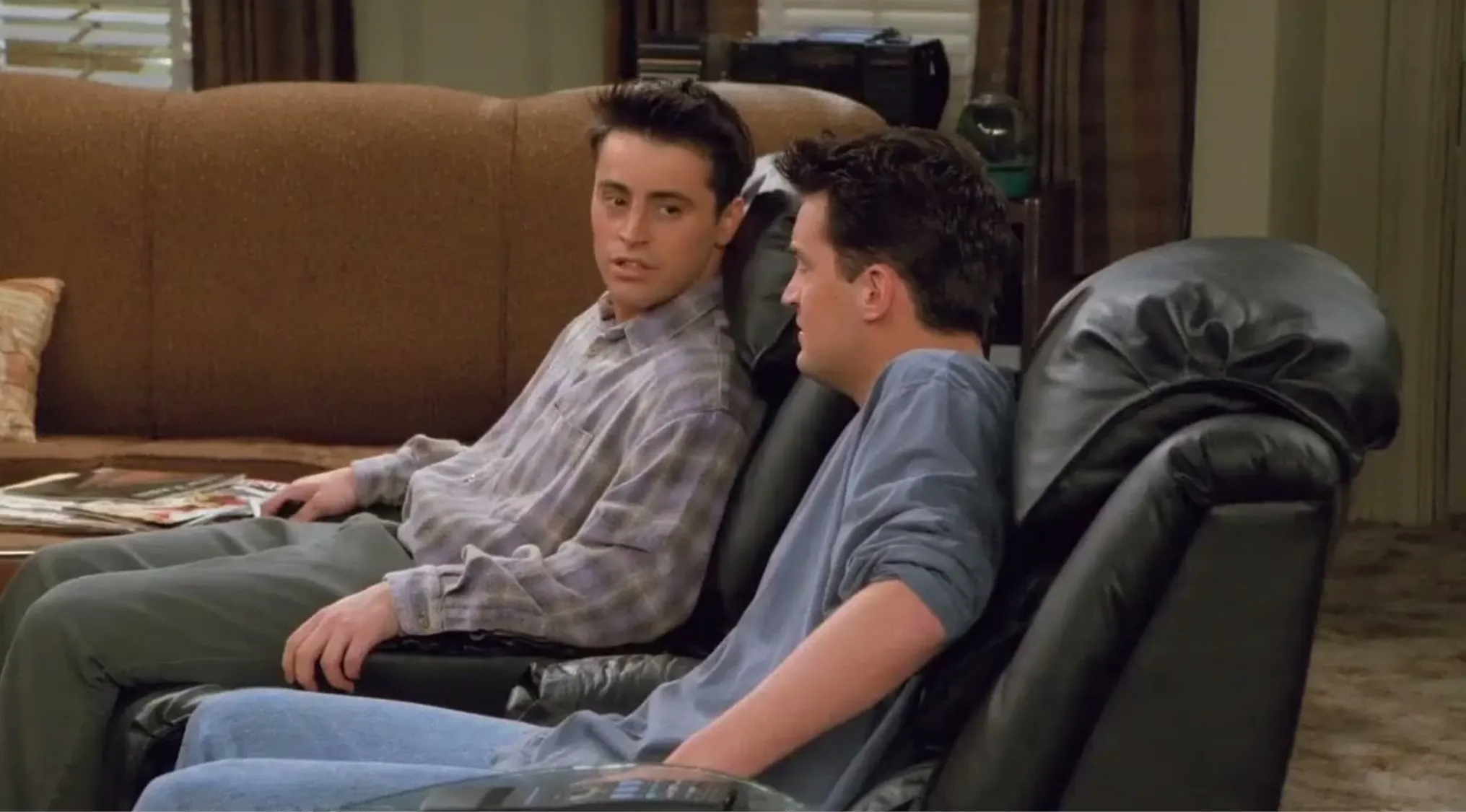 Joey and Chandler sitting on their black recliner chairs, discussing TV guide in Friends TV show scene.