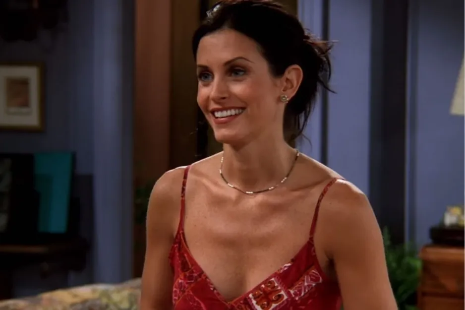 Monica smiling in a red dress indoors with dark hair tied back, from a popular TV sitcom scene.
