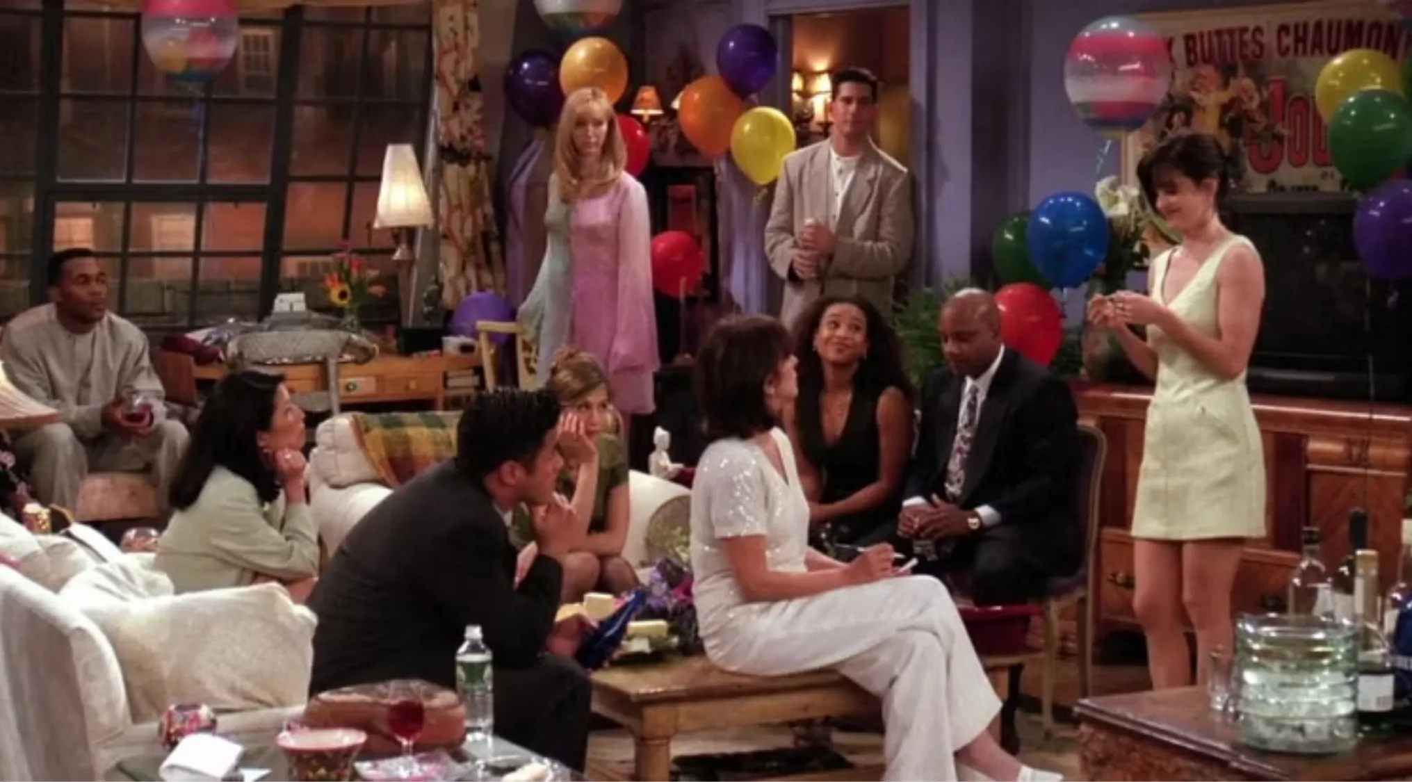 Friends fan birthday party scene with Monica, Phoebe, and group of friends surrounded by colorful balloons indoors.