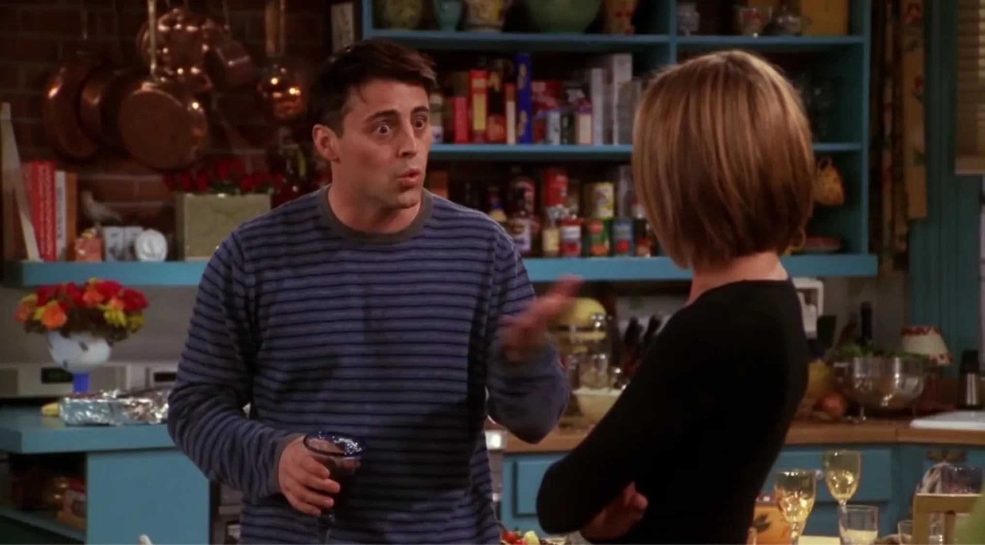 Joey from Friends explaining his idea of a moo point while holding a drink in a kitchen setting.