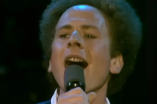 Singer performing Bridge Over Troubled Water by Simon and Garfunkel, close-up with microphone in hand on stage.