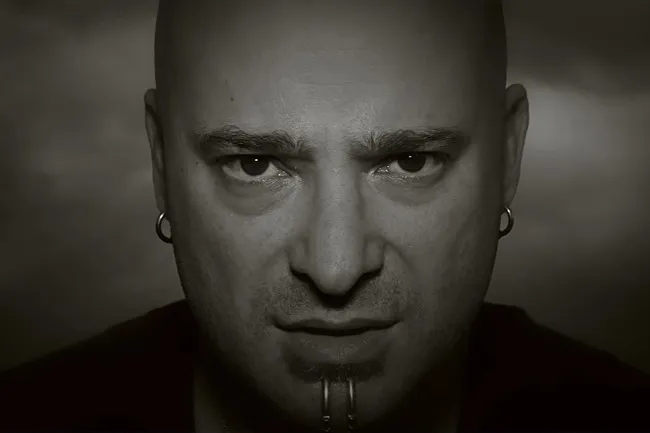 Close-up of a man with a serious expression, representing the song sound of silence by Disturbed and conflict style.