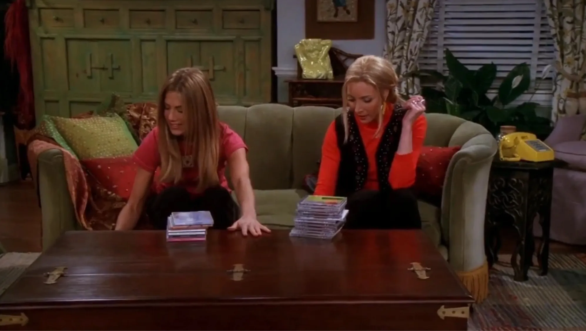 Two Friends characters sitting on a green couch sorting CD stacks, related to prove ultimate Friends fan quiz about Phoebe's hated store.