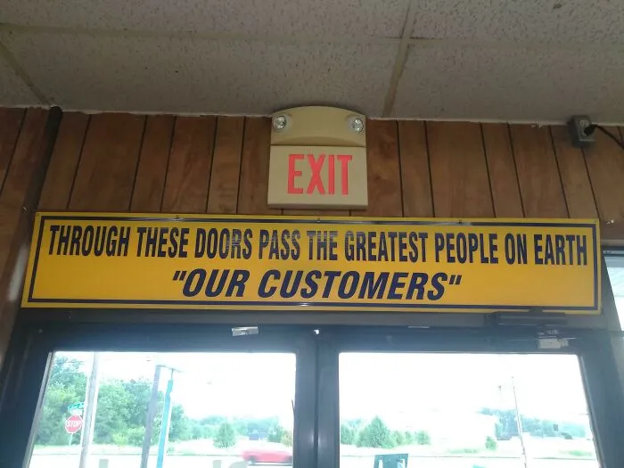 Yellow sign with quotation marks around the phrase our customers, humorously implying suspicious praise in a public entrance.