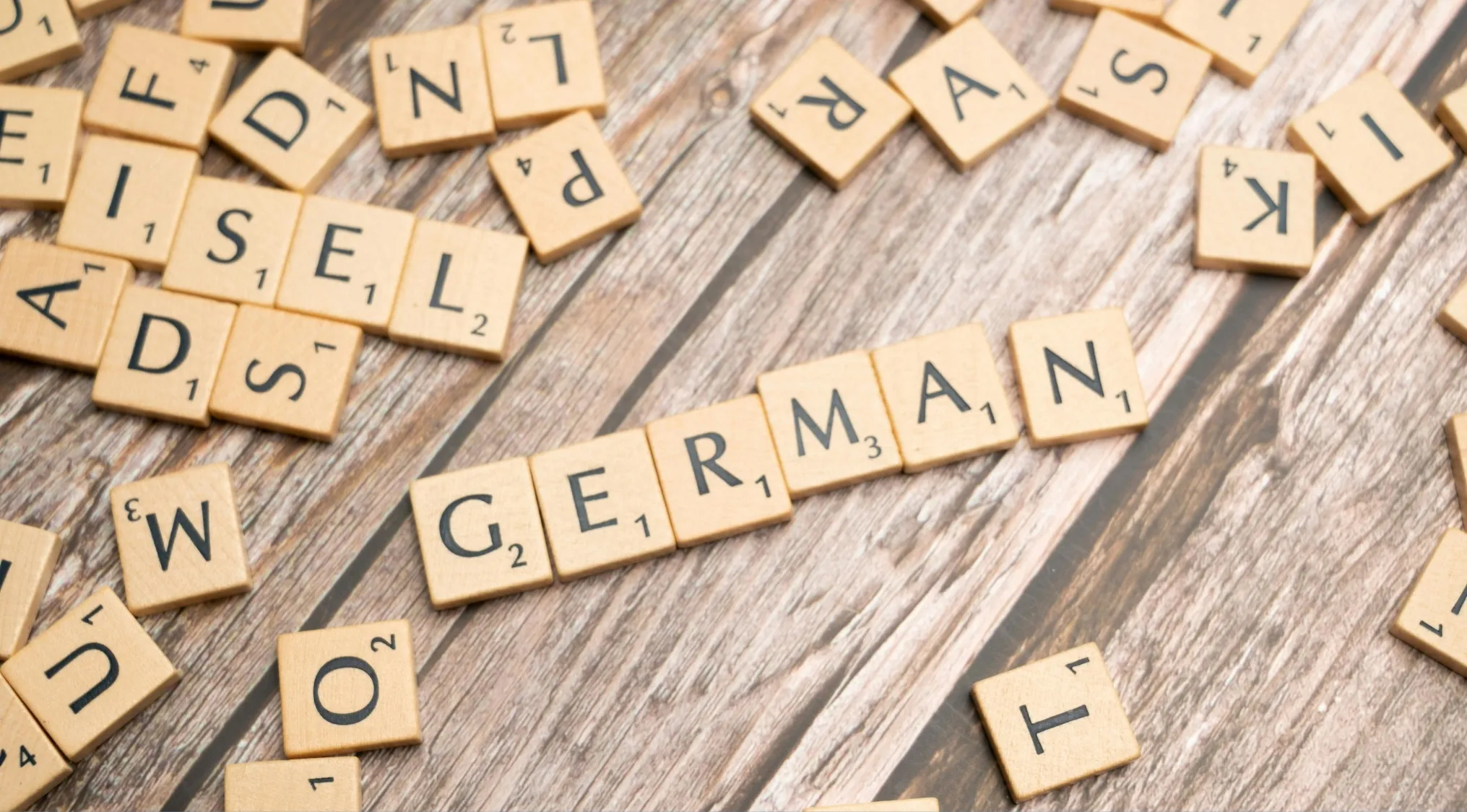 Scrabble tiles on wooden surface spelling German, related to countries with German as an official language in geography.